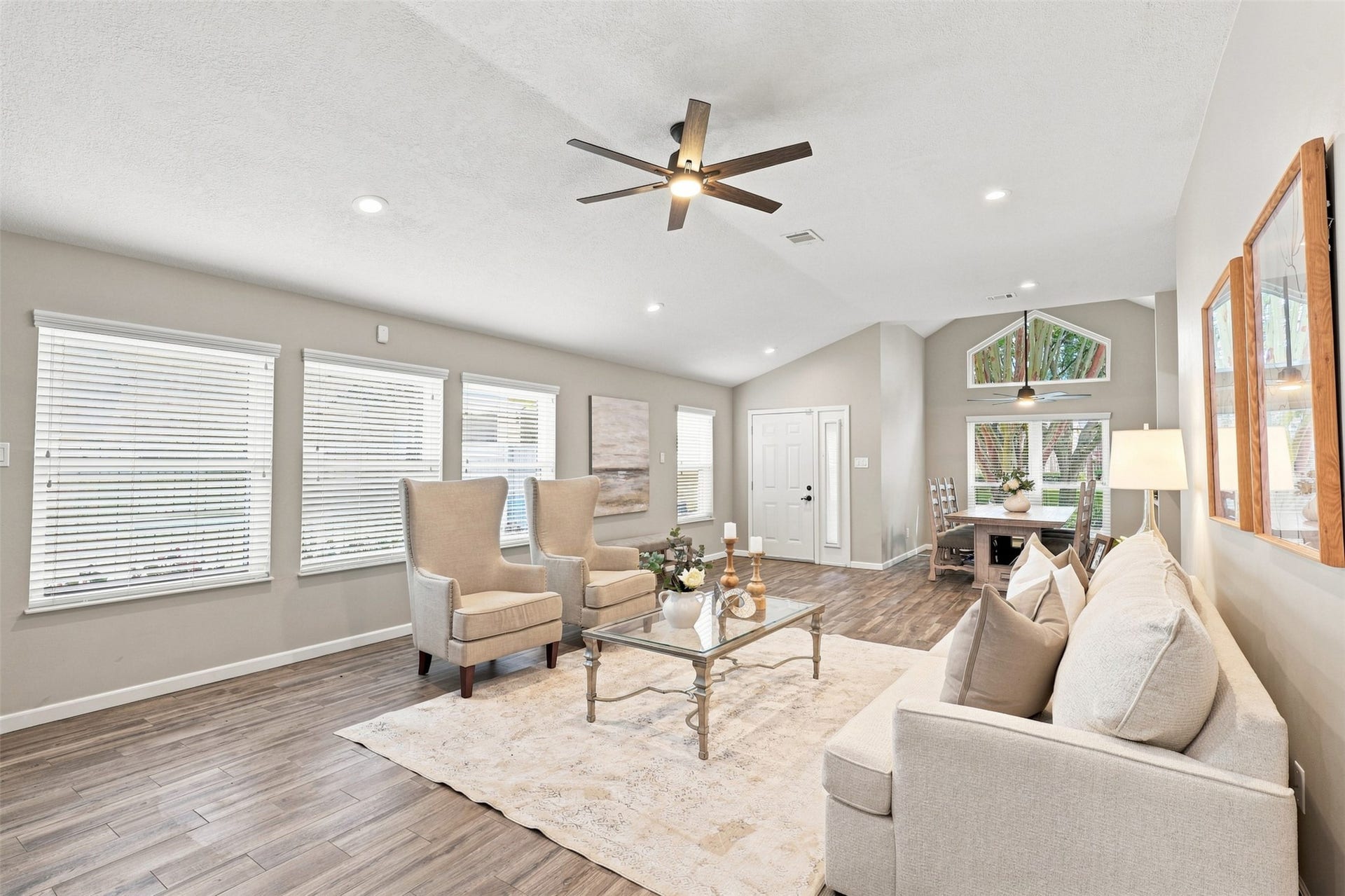 Bright, open living area featuring vaulted ceilings, abundant natural light, recessed lighting, wood-look flooring, and an easy flow into the dining space.