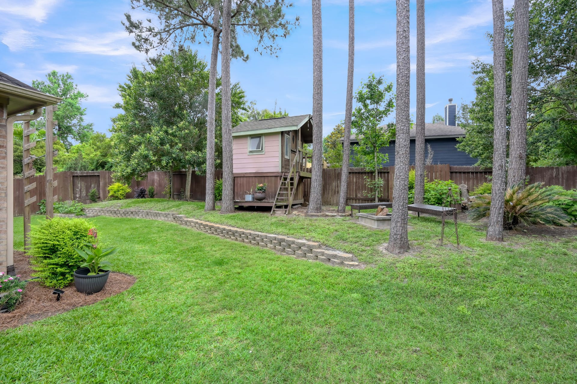 2502 Wynden Meadow Lane, Conroe, TX 77304 Charming backyard complete with a whimsical elevated playhouse, fire pit area, mature trees, and a park-like setting perfect for enjoying the outdoors.