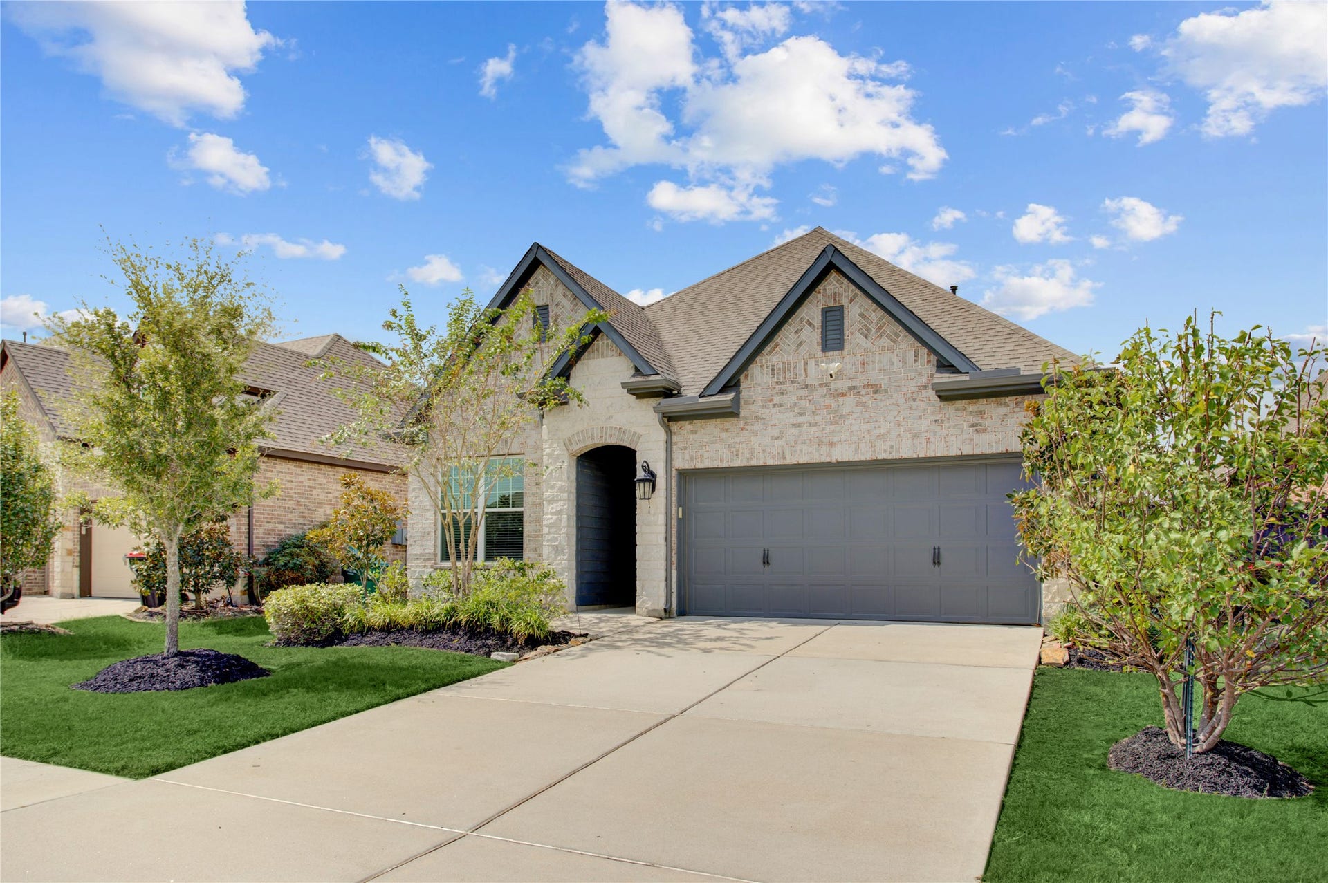3423 Tranquil Harvest Trail, Richmond, TX 77406 Well-manicured front exterior highlighting the homes brick faade, varied gabled rooflines, mature landscaping, and broad driveway.