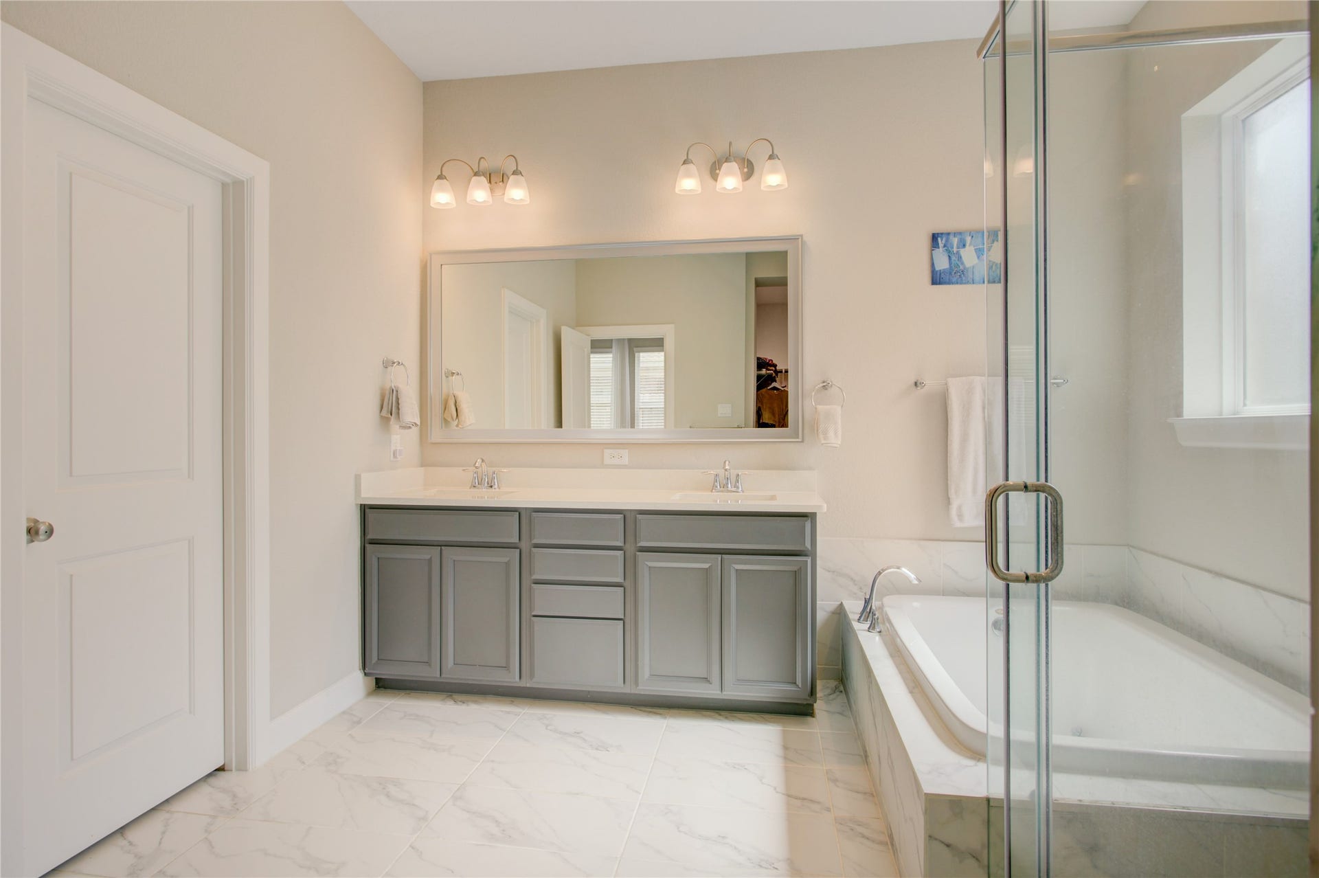 3423 Tranquil Harvest Trail, Richmond, TX 77406 Primary bathroom with a spacious dual-sink vanity, gray cabinetry, large mirror, and soaking tub with marble-look tile surround.