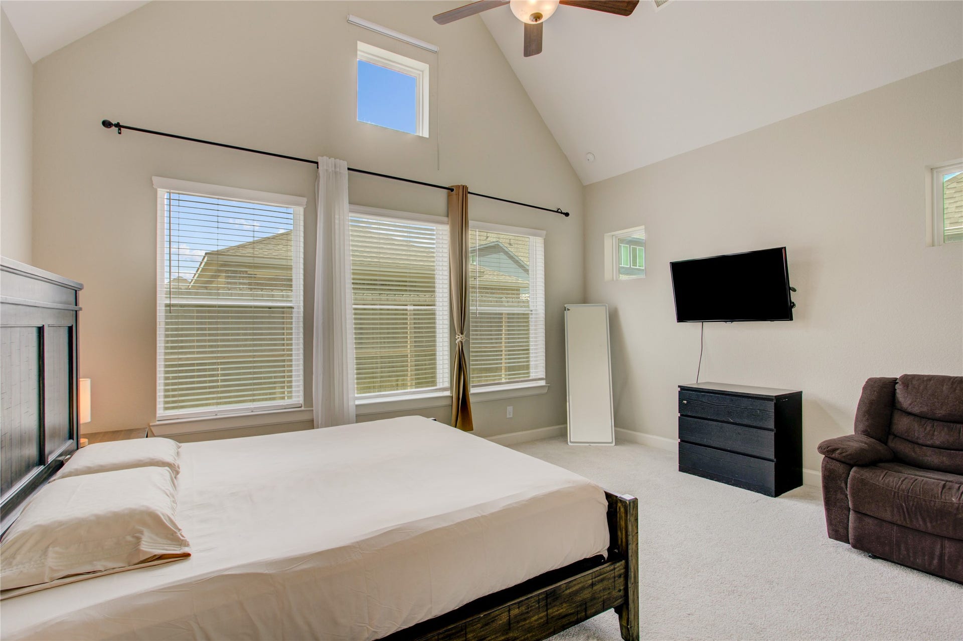 3423 Tranquil Harvest Trail, Richmond, TX 77406 Primary bedroom with a vaulted ceiling, multiple windows with blinds, ceiling fan, carpeted flooring, wall-mounted TV, dresser, and a separate recliner seating area.