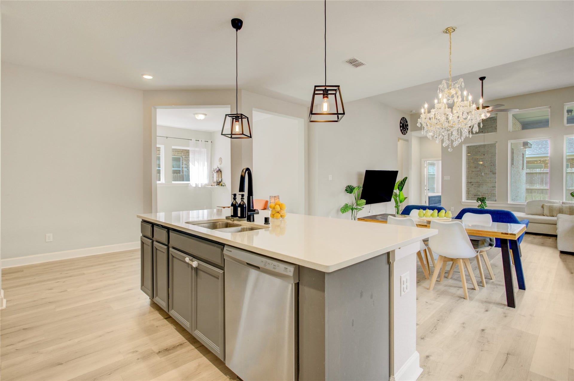 3423 Tranquil Harvest Trail, Richmond, TX 77406 Sleek kitchen highlighting the expansive quartz island, undermount sink, gray cabinetry, pendant lighting, and stainless steel dishwasher, with the dining and family areas visible beyond.