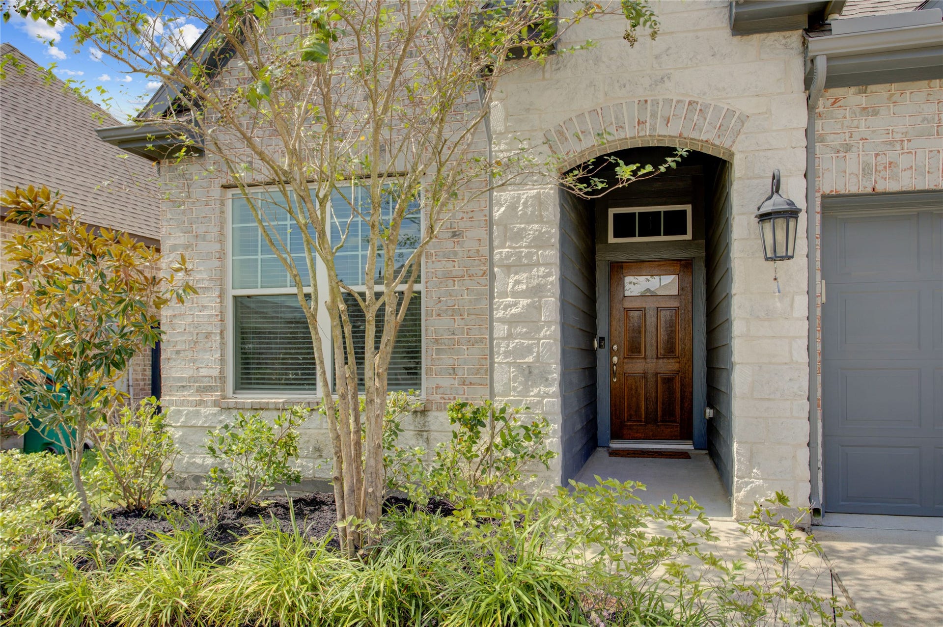 3423 Tranquil Harvest Trail, Richmond, TX 77406 Charming entryway highlighting the arched brick detailing, wood front door, front-facing window, exterior lantern, and landscaped planting bed.