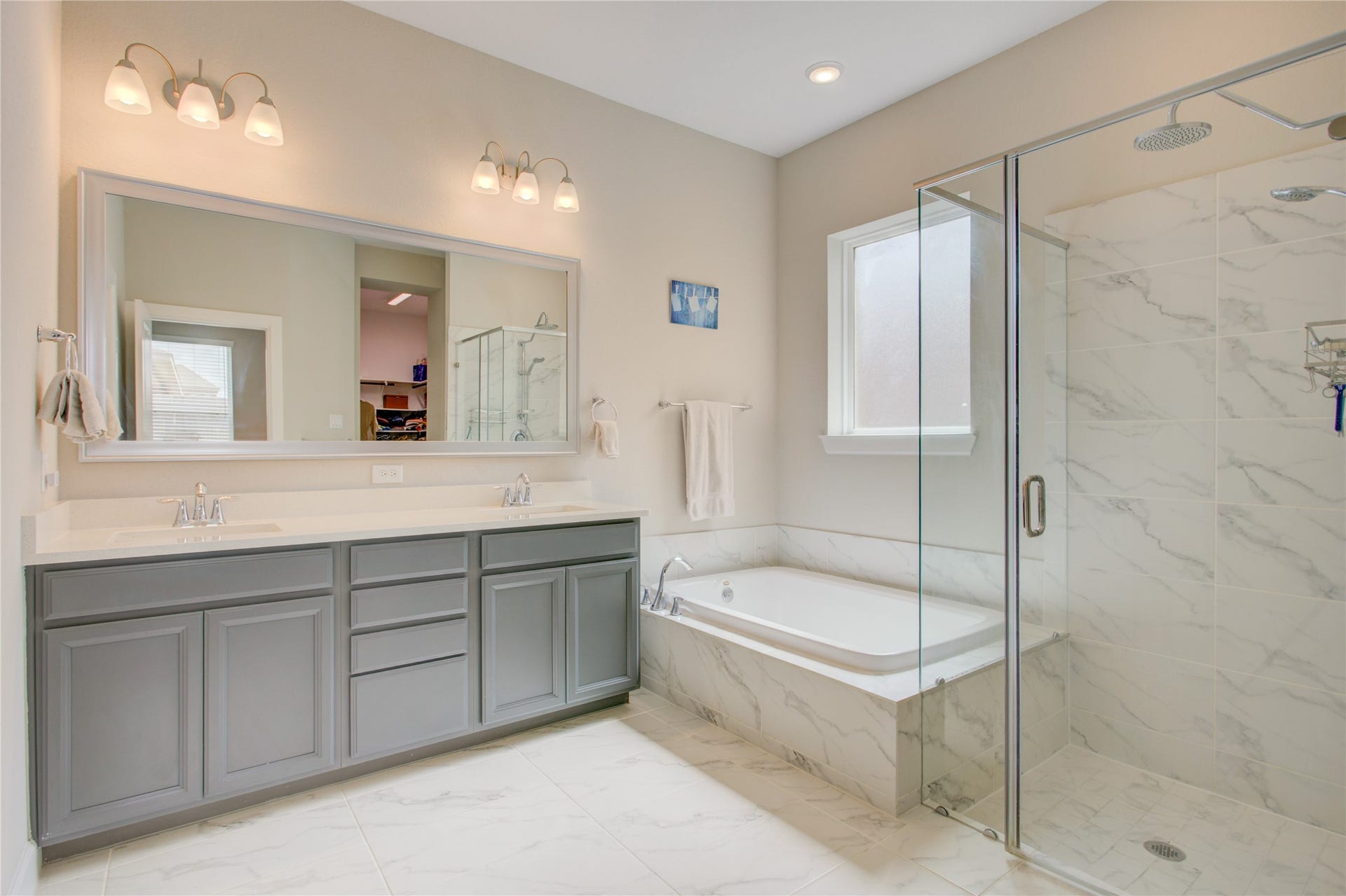 3423 Tranquil Harvest Trail, Richmond, TX 77406 Bright primary bathroom featuring a dual-sink vanity, gray cabinetry, soaking tub, and glass-enclosed walk-in shower with marble-look tile.