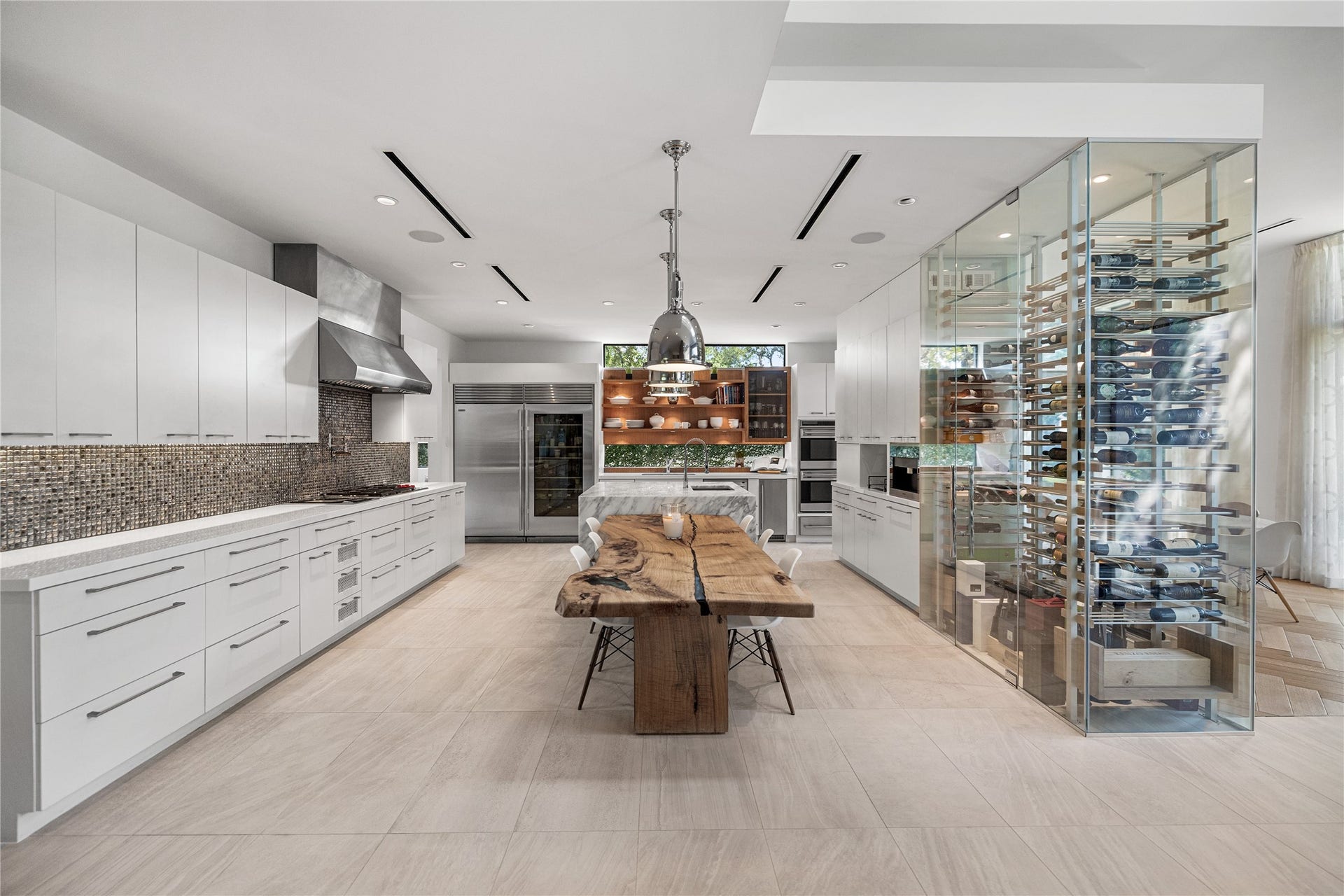 2608 Barbara Lane, Houston, TX 77005 Modern yet timeless, this sophisticated kitchen pairs a dramatic marble waterfall island and a beautifully curated, highly functional design. Commercial-grade appliances include a glass-door refrigerator, full-size freezer, double ovens, and a built-in Miele coffee system, creating a refined culinary space. The temperature-controlled glass wine room serves as a quiet divide between kitchen and formal dining.
