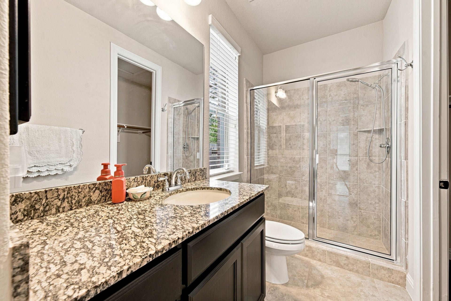 Private bath for the secondary bedroom, featuring a granite vanity, glass-enclosed shower, and adjoining walk-in closet.