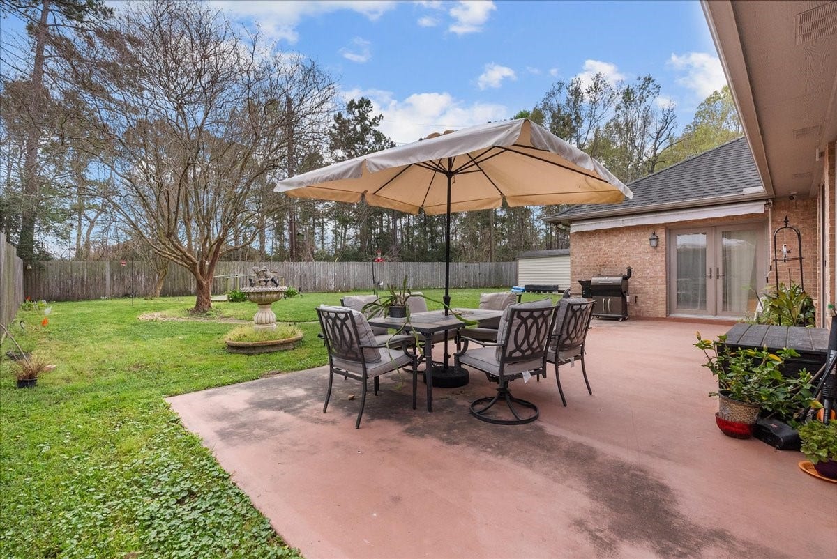 This photo showcases a spacious backyard with a large patio area featuring a dining set under a sturdy umbrella. There's a well-maintained lawn, mature trees, and a privacy fence, providing a serene outdoor setting perfect for relaxation and entertaining.
