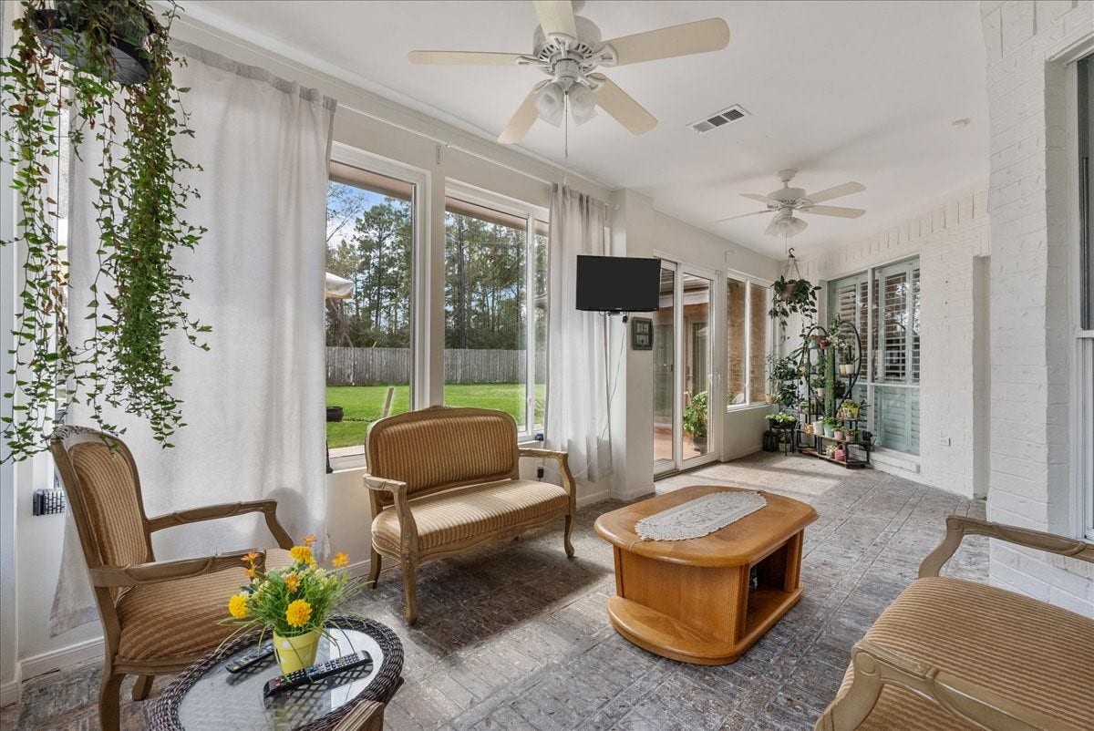 Bright sunroom with large windows, ceiling fans, and cozy atmosphere. Overlooks a lush backyard, perfect for relaxation and entertaining.
