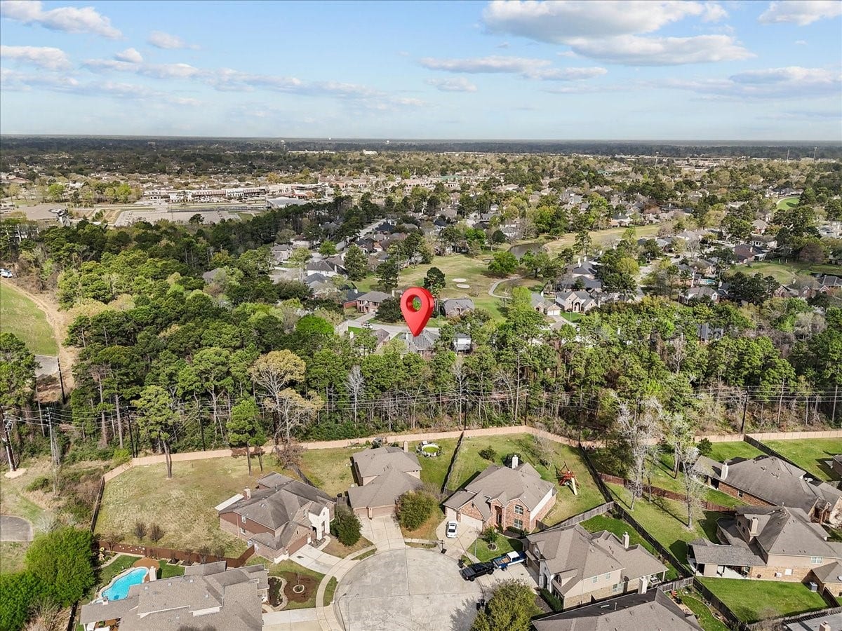 Aerial view of a suburban neighborhood surrounded by lush greenery. The area features spacious homes with ample yards, set in a quiet cul-de-sac. Nearby, a mix of wooded areas and open spaces offer a serene environment, with convenient access to local amenities.