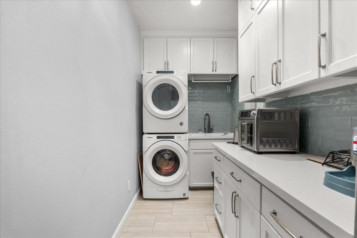This photo showcases a modern laundry room w ample white cabinetry, and a countertop. There's a sleek backsplash, a small sink, creating a functional and stylish space.