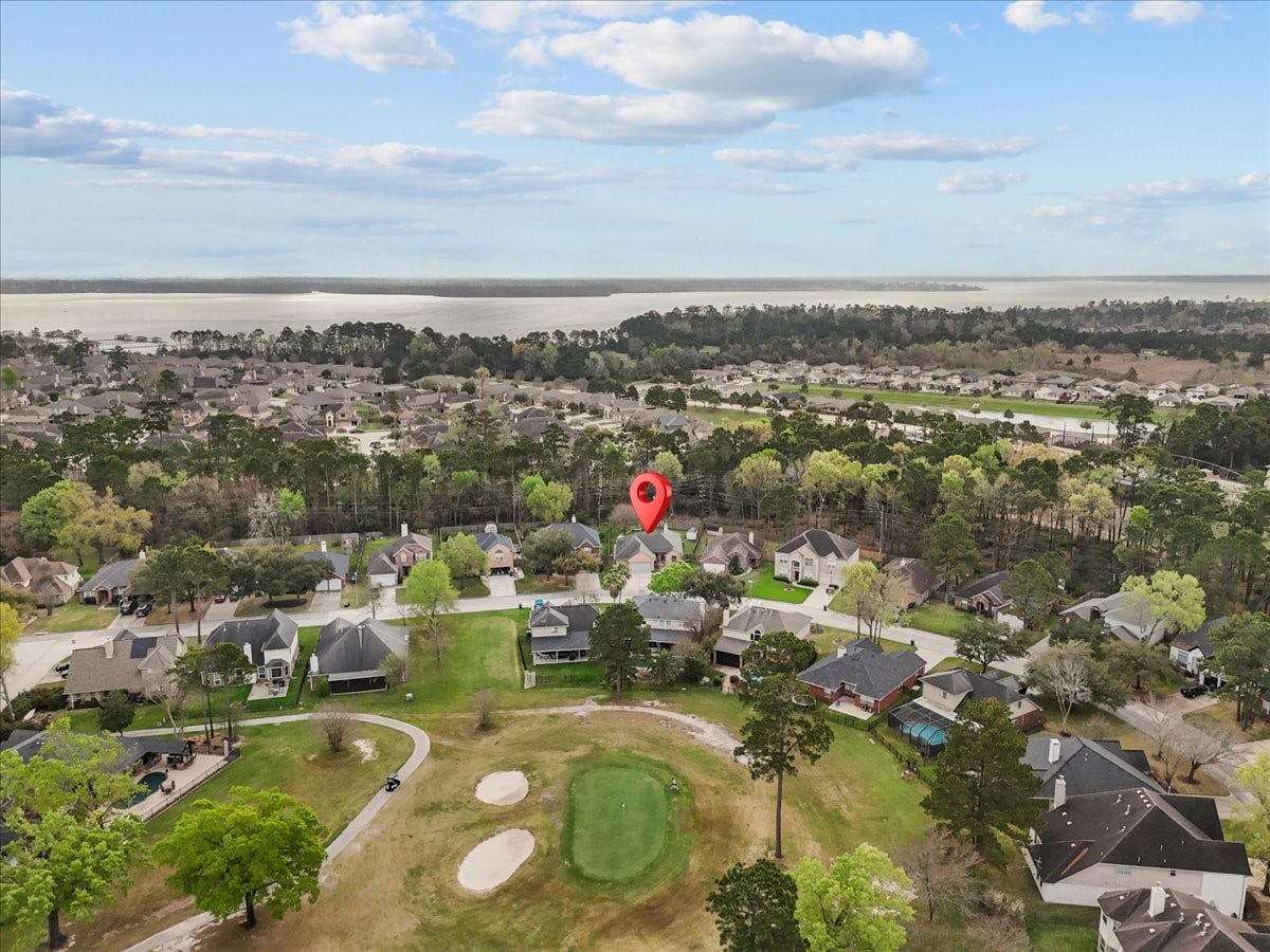This aerial photo showcases a tranquil neighborhood surrounded by lush greenery and a golf course. The area is characterized by spacious homes and a serene landscape, offering a scenic view of a nearby body of water. Ideal for those seeking a peaceful community with recreational amenities.