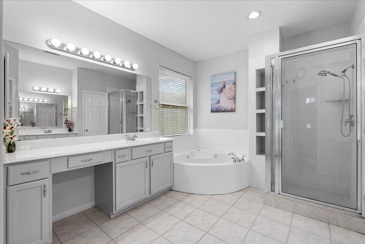 Spacious bathroom with a large vanity and ample storage, featuring a luxurious corner bathtub and a separate glass-enclosed shower. The room is well-lit, with neutral tiles and a window for natural light.