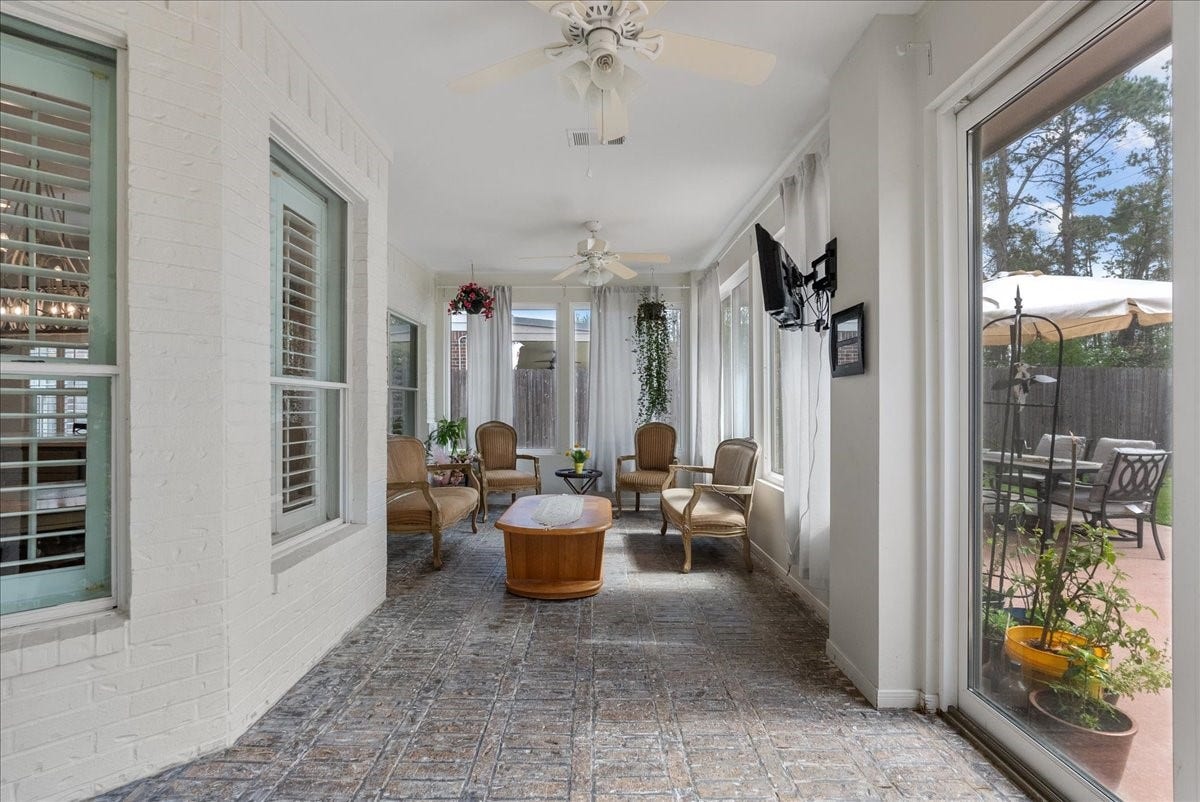 This inviting sunroom features large windows, ceiling fans, and relaxing view, offering a bright, airy space perfect for relaxation. It opens to a patio area, ideal for outdoor entertaining.