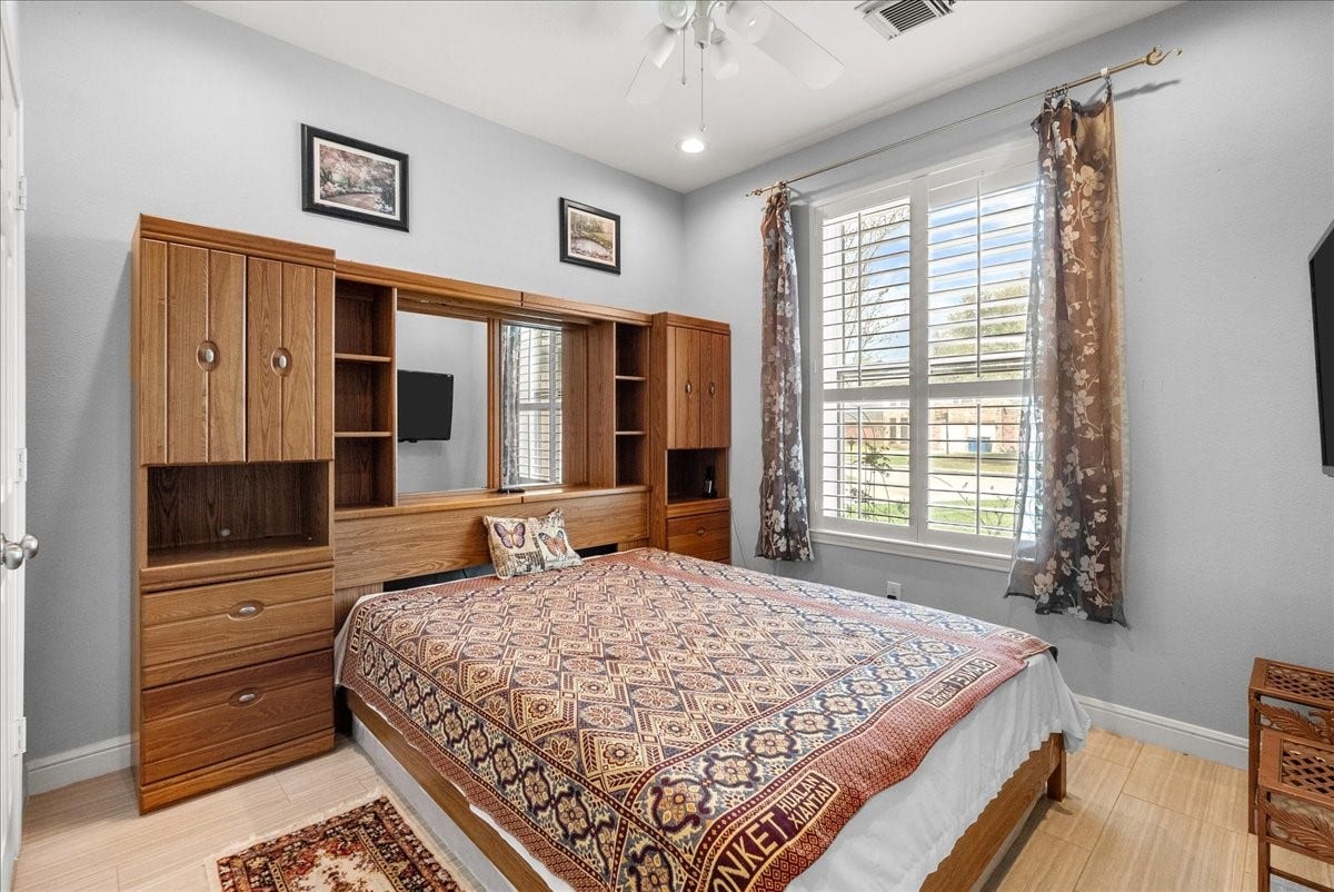 This cozy bedroom features a large window with shutters, allowing plenty of natural light. It has a built-in wooden storage unit around the bed, complementing the room's warm and inviting decor.
