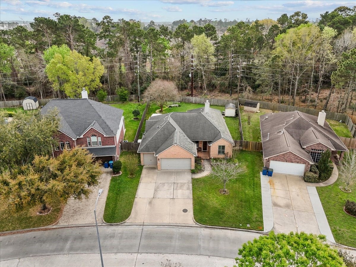 This aerial photo showcases a charming suburban neighborhood with three single-family homes, each with well-maintained lawns and driveways. The area is surrounded by lush greenery and mature trees, offering a sense of privacy and tranquility. The homes are situated on a quiet street, ideal for families.