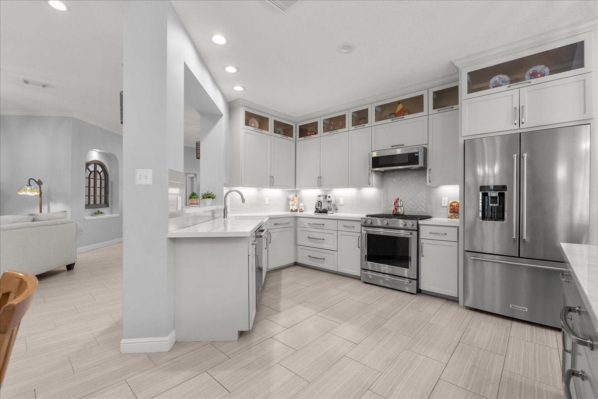 This modern kitchen features sleek white cabinetry, stainless steel appliances, and ample counter space. The open layout connects seamlessly to a cozy living area, enhanced by neutral tones and recessed lighting for a bright, inviting atmosphere.
