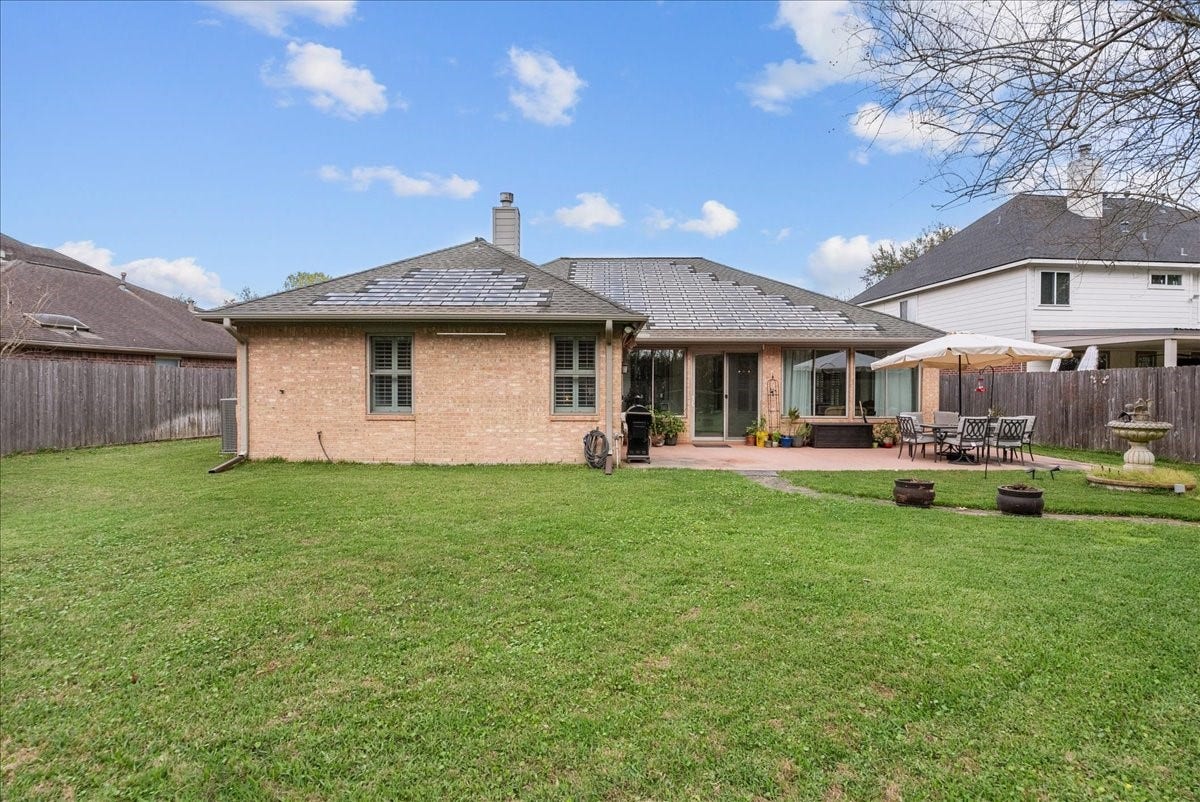 This photo showcases a single-story brick home with a spacious backyard, featuring a well-maintained lawn, a patio area with outdoor seating, and a fenced perimeter for privacy. Perfect for outdoor entertaining and relaxation.