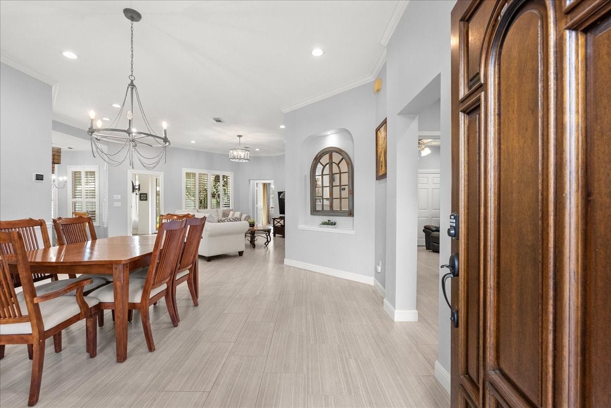 This inviting home features an open-concept layout with a spacious dining area, elegant chandelier, and light wood flooring. The living area is bright, with large windows and neutral tones, providing a warm and welcoming atmosphere.