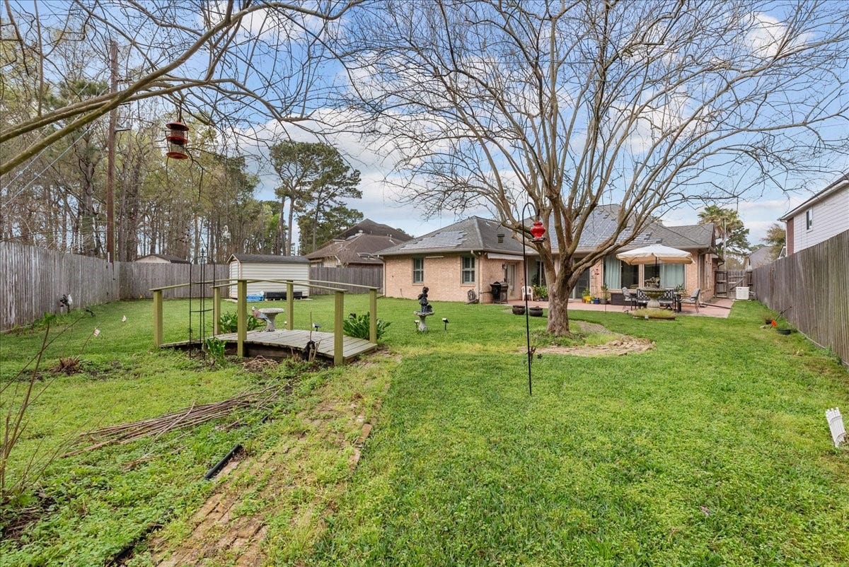 Spacious backyard with a mature tree and a wooden deck, perfect for outdoor gatherings. The area is fenced for privacy and features a patio with seating, creating a cozy and inviting atmosphere.
