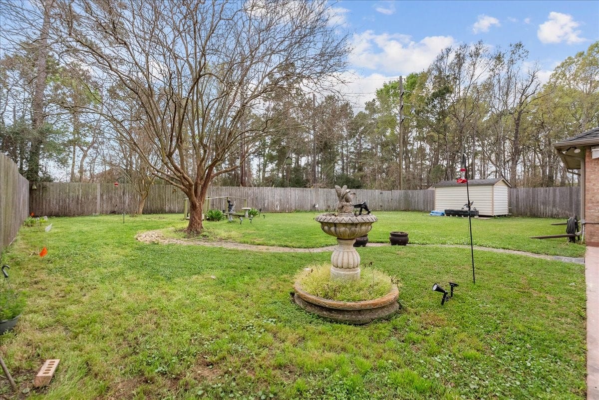 This spacious backyard features a well-maintained lawn, mature trees, and a charming central fountain. It includes a storage shed, surrounded by a wooden privacy fence, perfect for outdoor activities and relaxation.