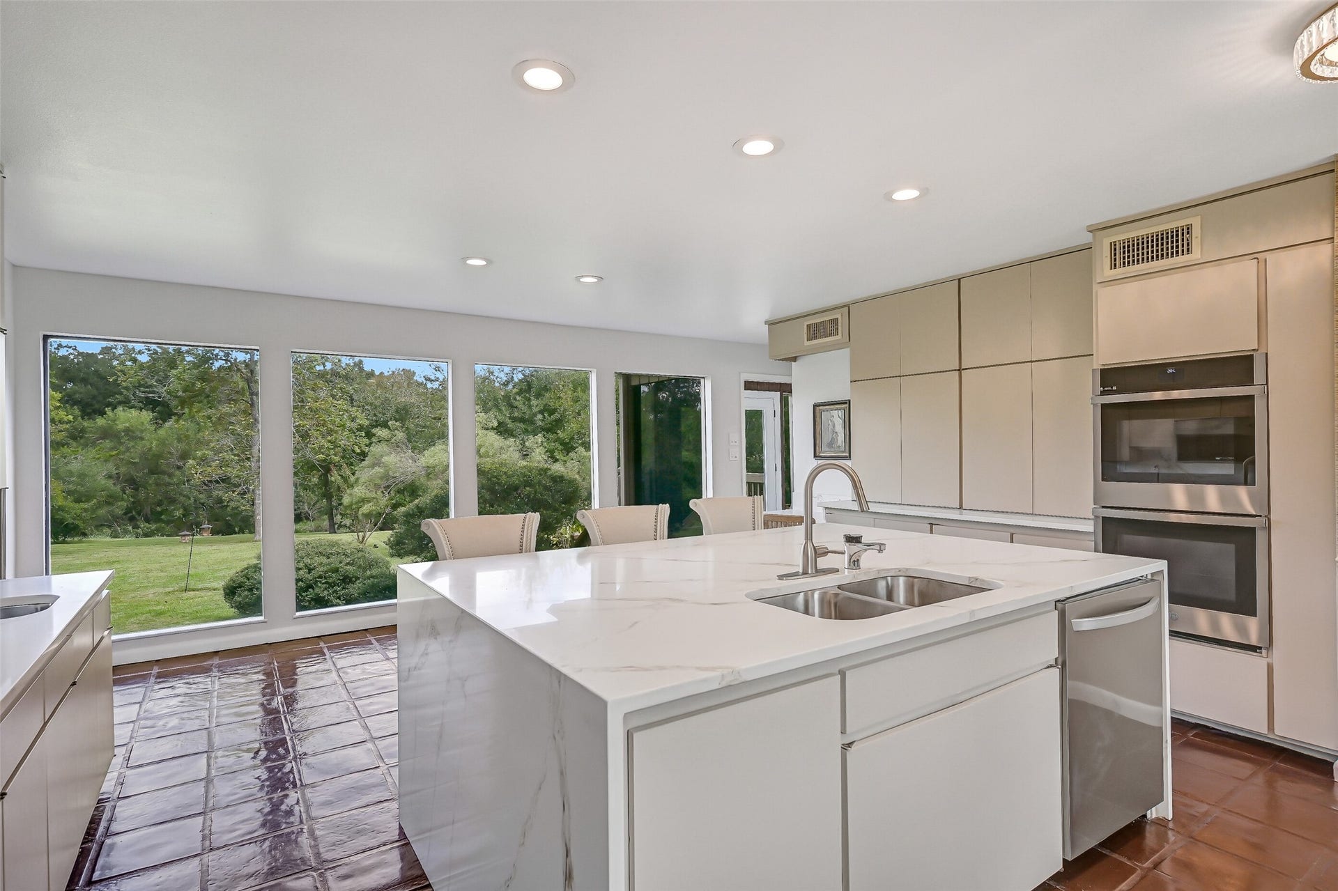 300 Courtlandt Place, Friendswood, TX 77546 A series of oversized picture windows stretches along the rear of the kitchen, showcasing beautiful views of the expansive lawn & mature trees. The painted tile flooring continues into this light-filled area, which connects the renovated kitchen to the home's adjoining living spaces.