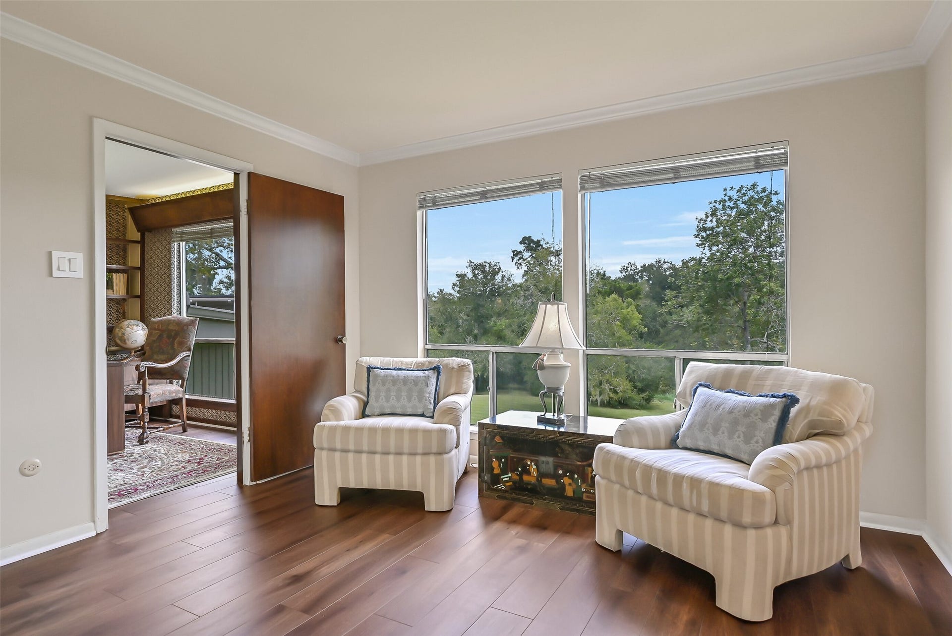 300 Courtlandt Place, Friendswood, TX 77546 A comfortable sitting area within the upstairs primary suite enjoys beautiful treetop views through two large windows overlooking the acreage. Wood-look flooring, crown molding & neutral finishes create a welcoming space for reading or relaxing, with the adjoining library/office just beyond the doorway.