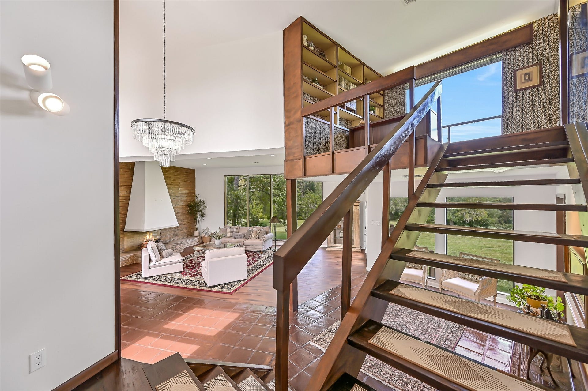 300 Courtlandt Place, Friendswood, TX 77546 The distinctive open-riser wooden staircase leads from the grand entry to the home's private upper level, reserved for the primary suite & adjoining study. An elevated library with built-in shelving overlooks the living room, while expansive windows & a dramatic chandelier accentuate the open design.