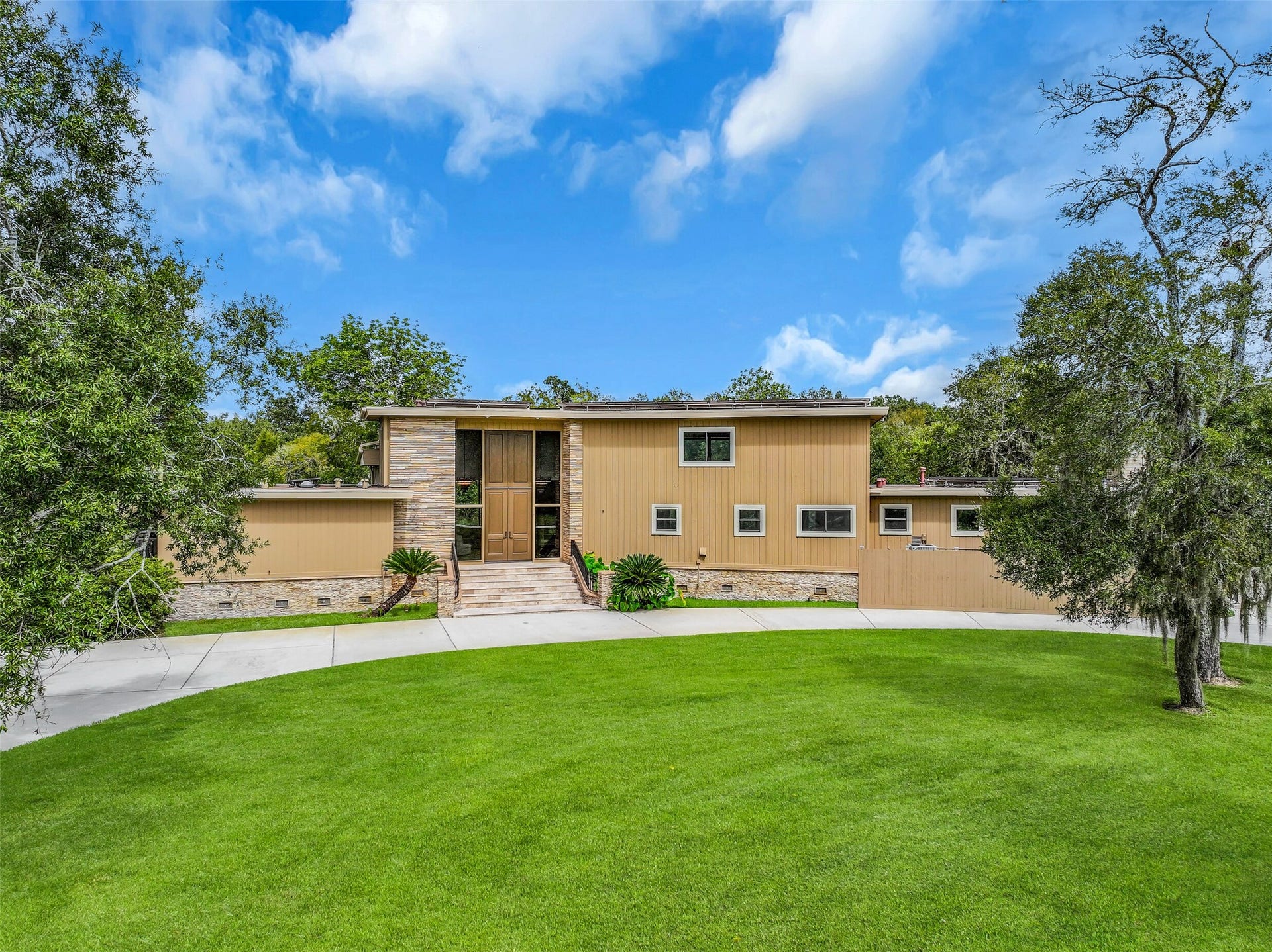 300 Courtlandt Place, Friendswood, TX 77546 An inviting approach showcases the home's unique architectural design, with stone exterior accents, tall double entry doors & extensive windows. The grand entrance is reached by a travertine staircase with iron railings, creating a memorable introduction to this one-of-a-kind property.