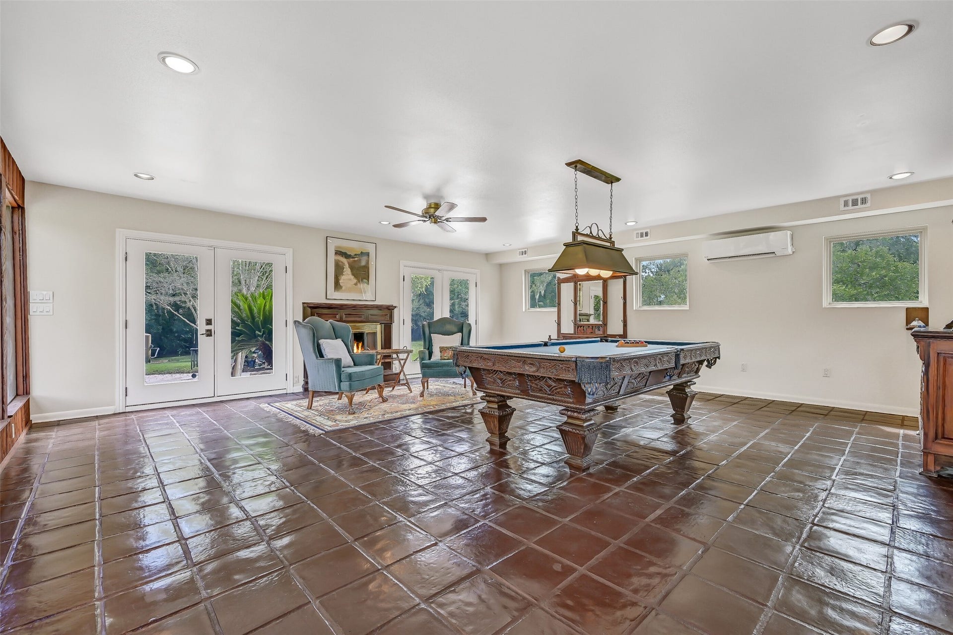 300 Courtlandt Place, Friendswood, TX 77546 The gameroom's generous dimensions are especially apparent from this angle, with plenty of open floor space surrounding the pool table. Two sets of French doors are visible, providing direct outdoor access, while a gas-log fireplace, supplemental mini-split A/C & recessed lighting add comfort.
