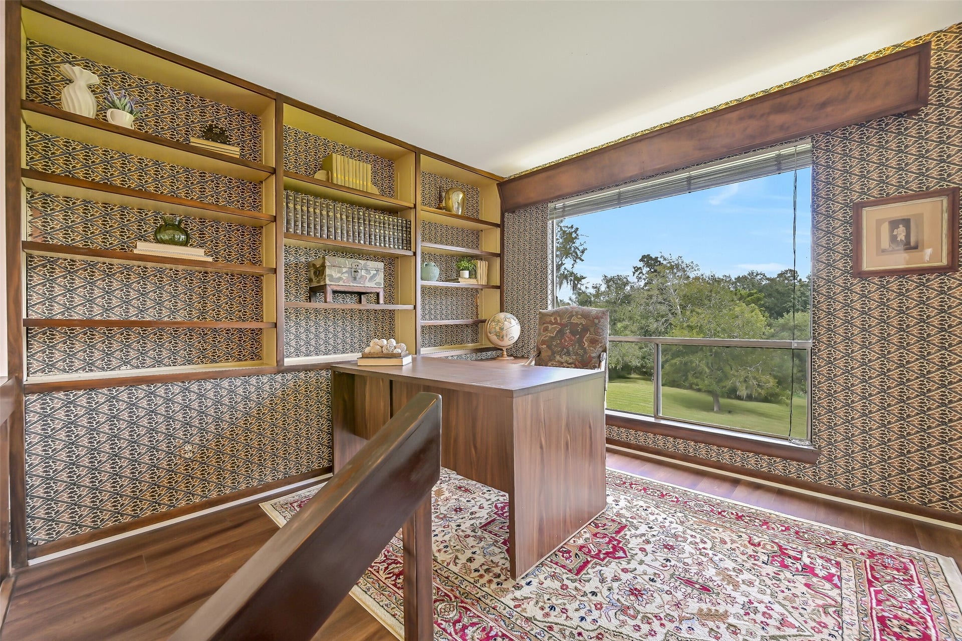 300 Courtlandt Place, Friendswood, TX 77546 Perched above the main living area, this 10' x 11' library/office features a wall of custom built-in bookshelves, decorative patterned wallpaper & wood-look flooring. A large picture window overlooks the property's mature trees & sprawling grounds, creating a quiet, light-filled workspace.