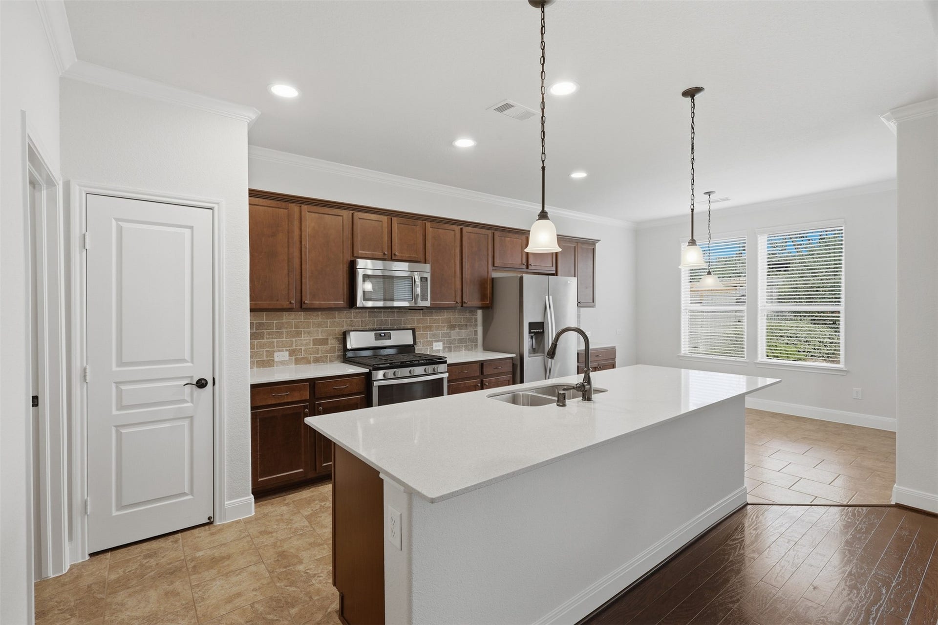 677 Tenuta Lane, League City, TX 77573 Open island kitchen with quartz countertops, stainless steel appliances, abundant cabinetry, recessed lighting, and breakfast area, all flowing seamlessly into the dining and living spaces.