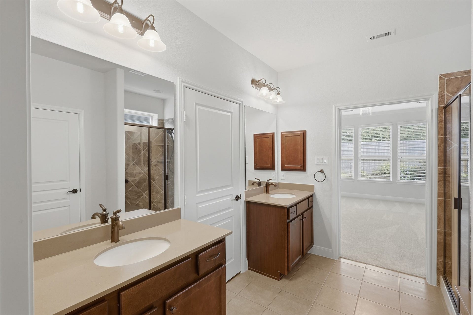 677 Tenuta Lane, League City, TX 77573 Primary bathroom featuring separate vanities, generous counter space, and an oversized walk-in shower with tile, glass enclosure, and built-in bench. The large walk-in closet provides excellent storage and convenient access directly from the primary bath.