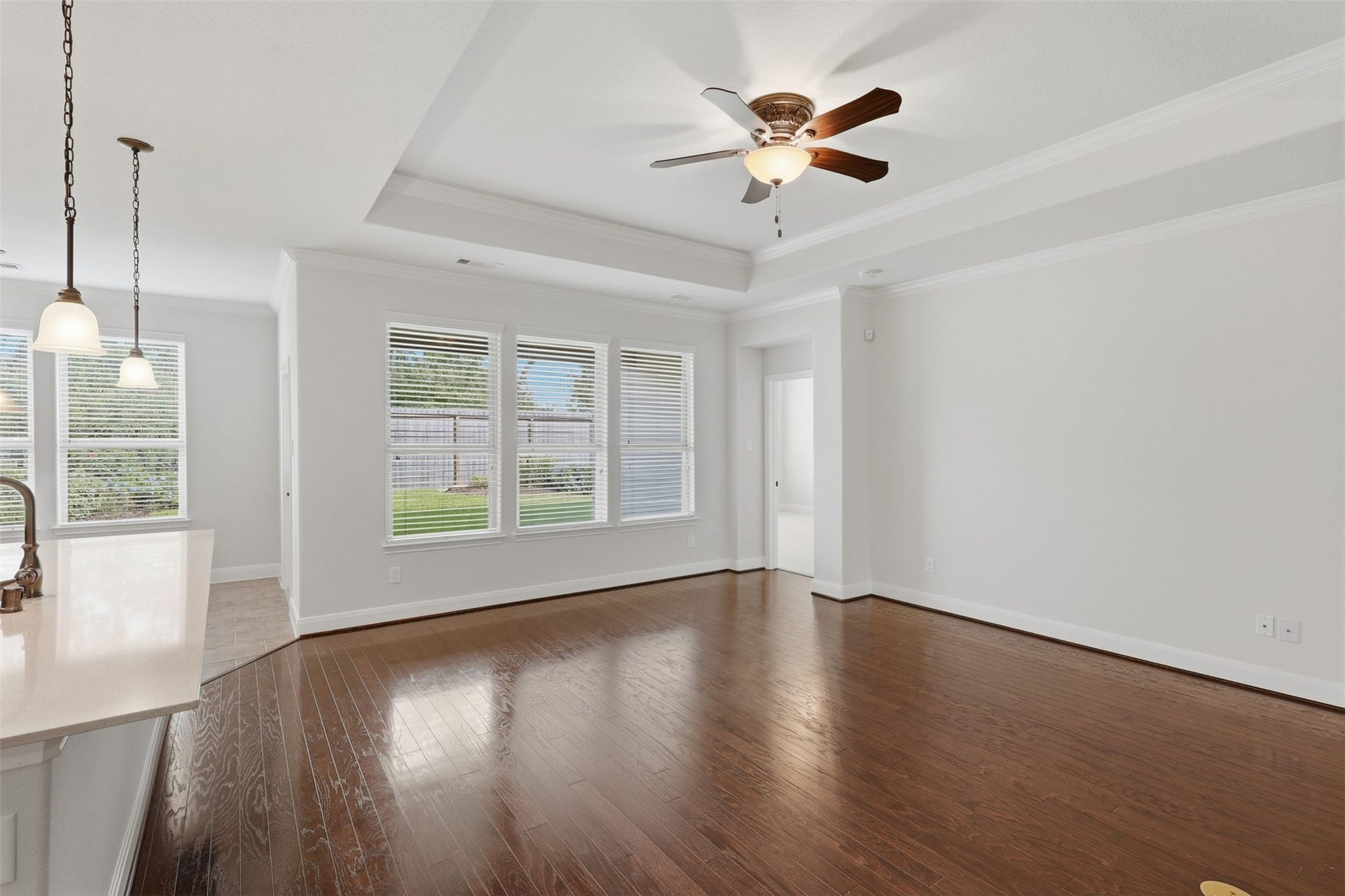 677 Tenuta Lane, League City, TX 77573 Spacious, light-filled living room featuring beautiful hardwood flooring, crown molding, a tray ceiling, ceiling fan, and a wall of windows overlooking the backyard.
