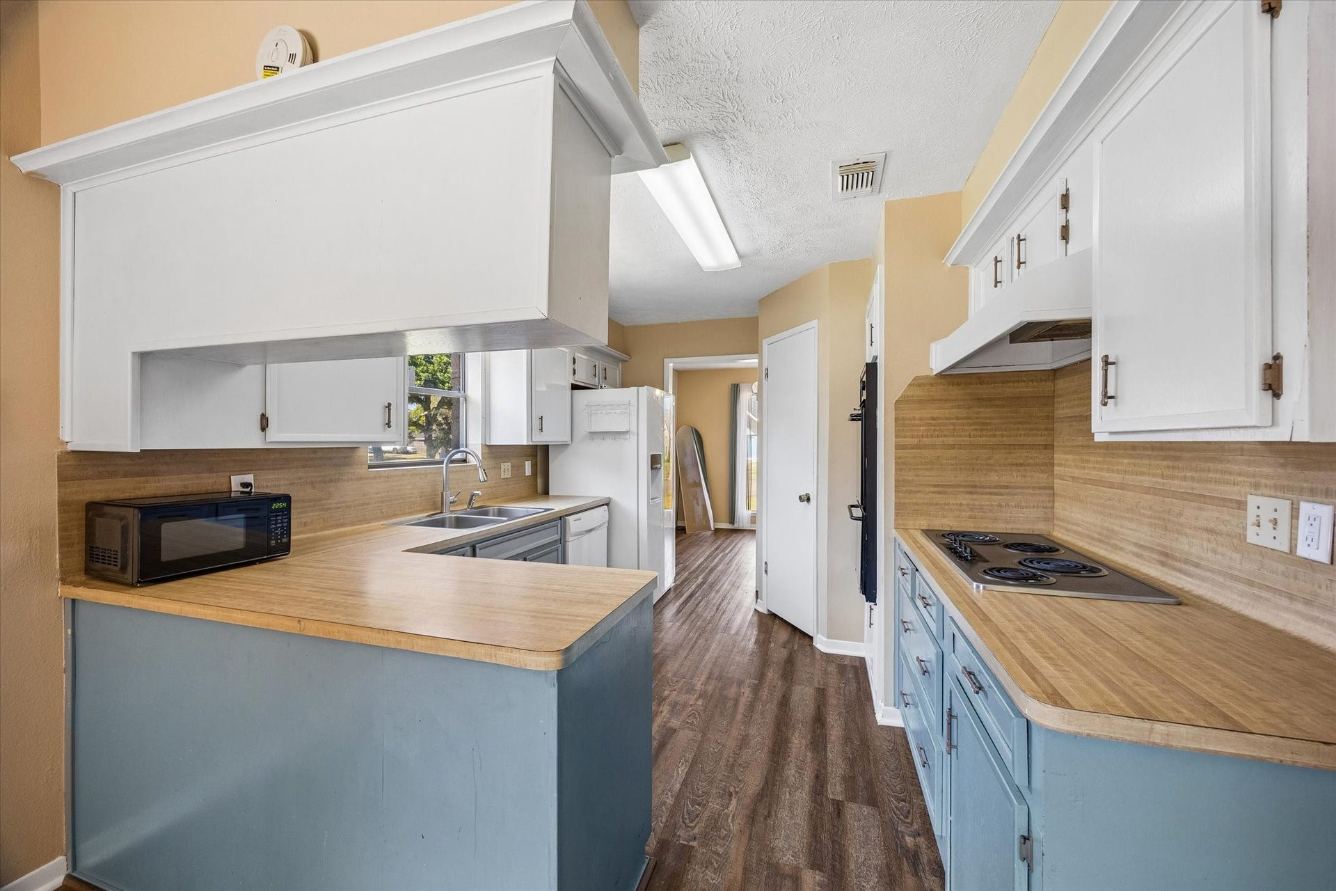 10110 Sagemill Drive, Houston, TX 77089 Charming kitchen with a cozy layout featuring white cabinetry and a convenient breakfast bar. The space is accented by warm-toned walls and natural light from a window above the sink.