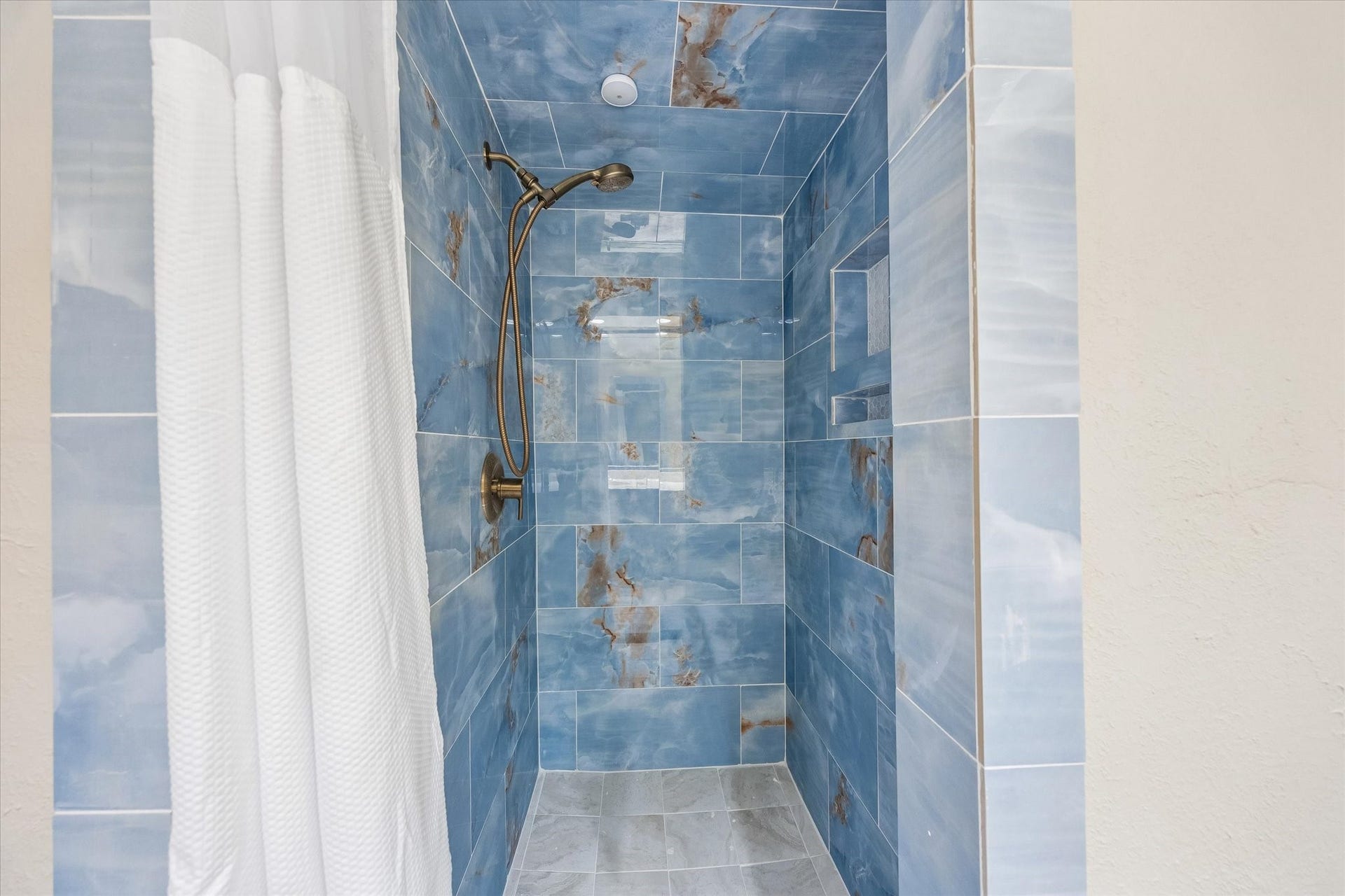 10110 Sagemill Drive, Houston, TX 77089 Luxurious shower with stunning blue marble-like tiles and a sleek bronze showerhead, offering a serene spa-like experience.