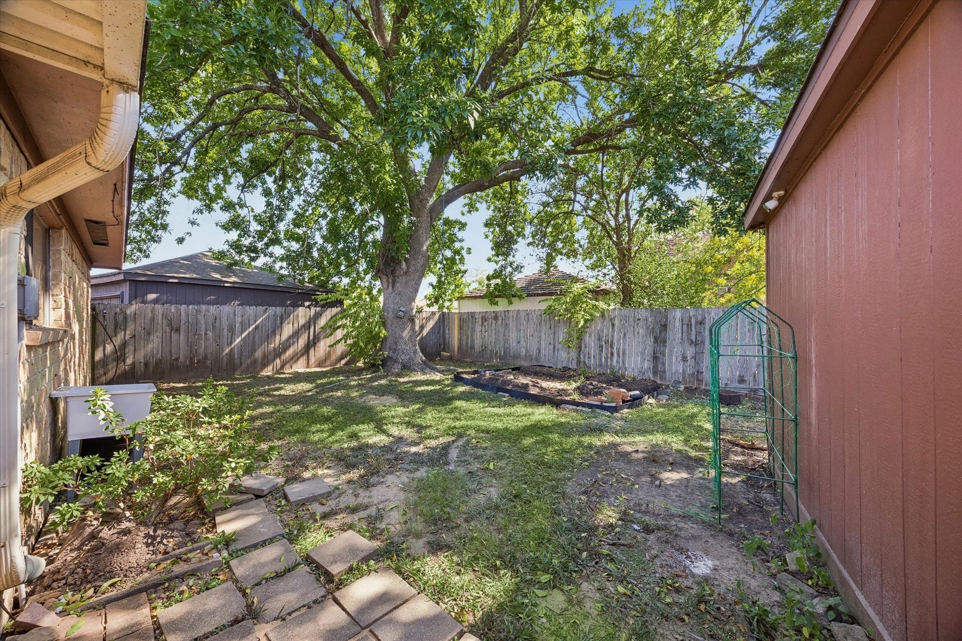 10110 Sagemill Drive, Houston, TX 77089 Charming backyard with a large, shady tree and ample space for gardening or relaxation, enclosed by a wooden fence for privacy.