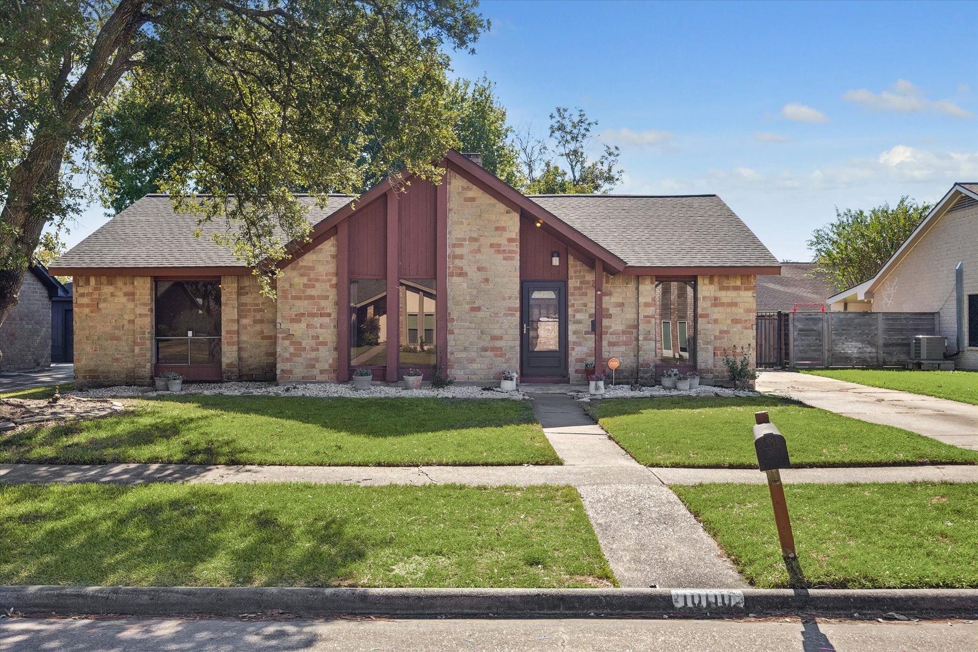 10110 Sagemill Drive, Houston, TX 77089 Charming brick home with a unique peaked roof and expansive windows, nestled under the shade of mature trees, offering a welcoming front walkway and lush lawn.