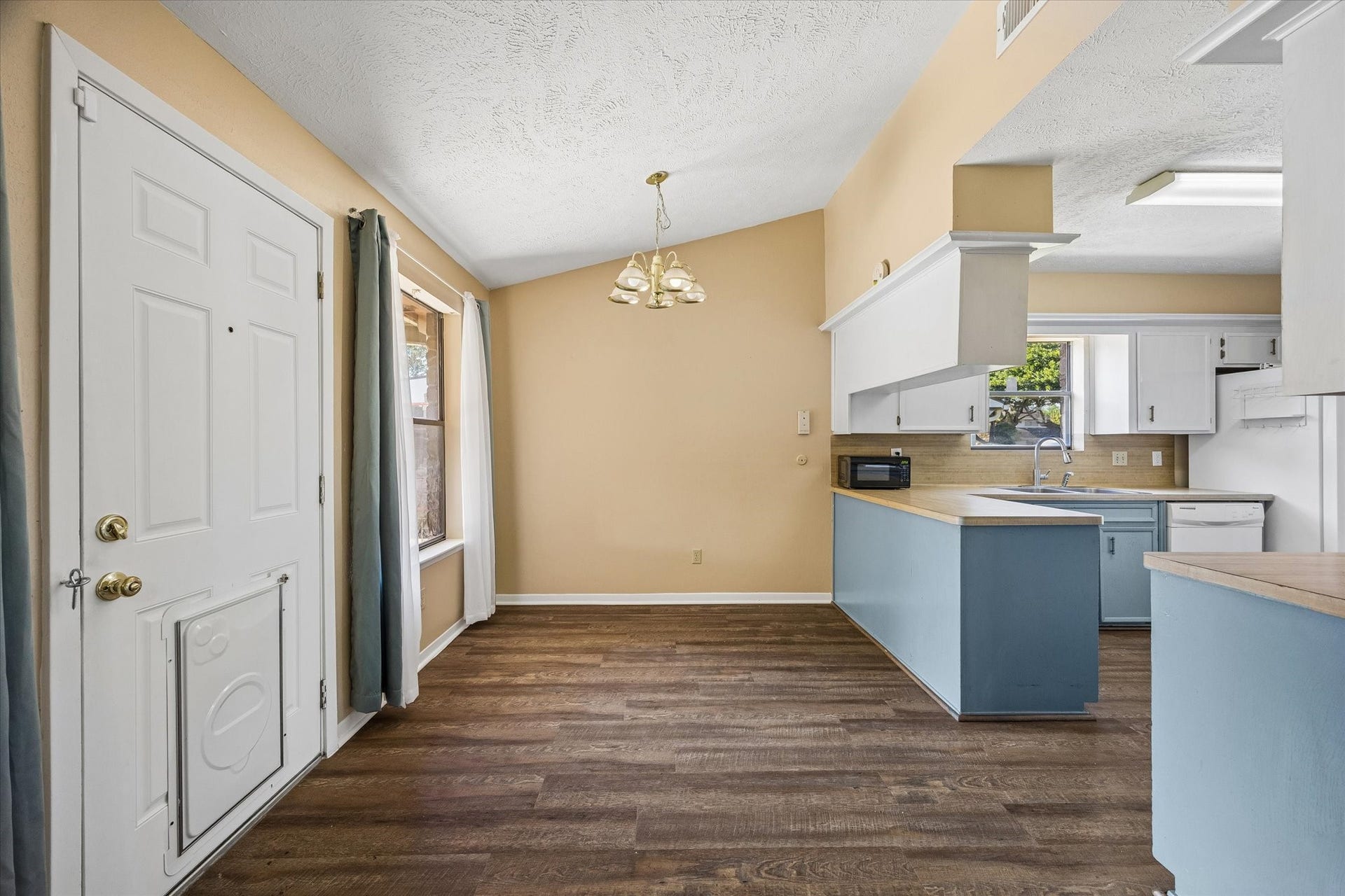 10110 Sagemill Drive, Houston, TX 77089 Charming open-concept kitchen and dining area featuring a vaulted ceiling, warm flooring, and ample natural light, with stylish blue cabinetry and a cozy chandelier.