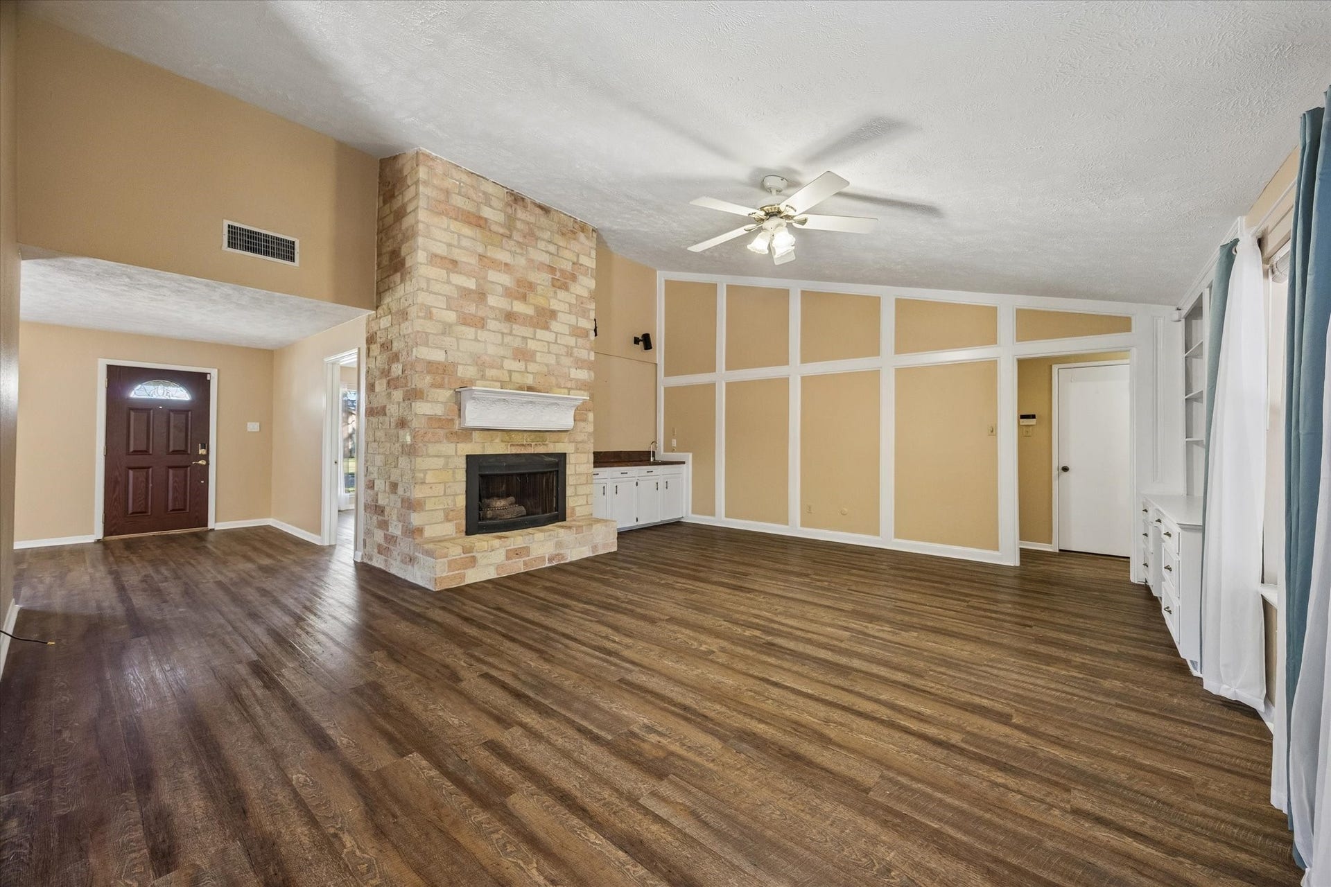 10110 Sagemill Drive, Houston, TX 77089 Spacious living room with rich floors and a striking brick fireplace, perfect for cozy evenings. Elegant built-in shelving adds character, while large windows fill the space with natural light.