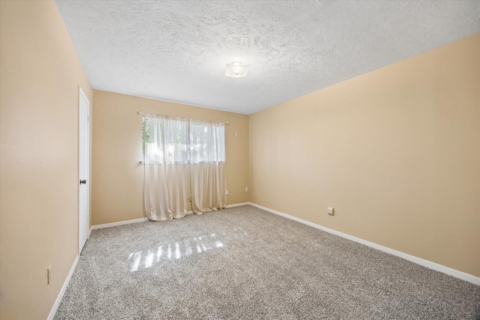 10110 Sagemill Drive, Houston, TX 77089 Spacious room with soft beige walls, plush carpeting, and ample natural light streaming through a large window with sheer curtains.