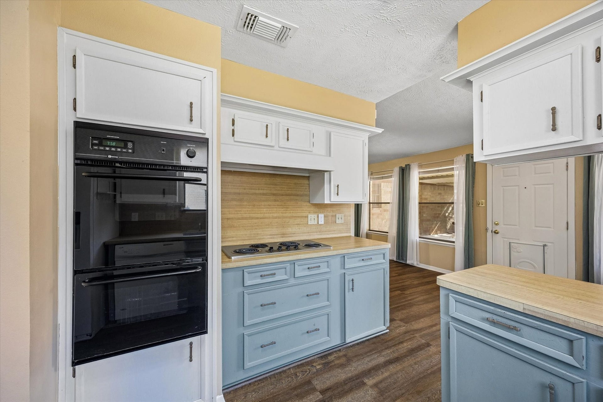 10110 Sagemill Drive, Houston, TX 77089 Charming kitchen with retro flair features a double oven, electric cooktop, and a blend of white and blue cabinetry, complemented by warm wood accents and natural light.