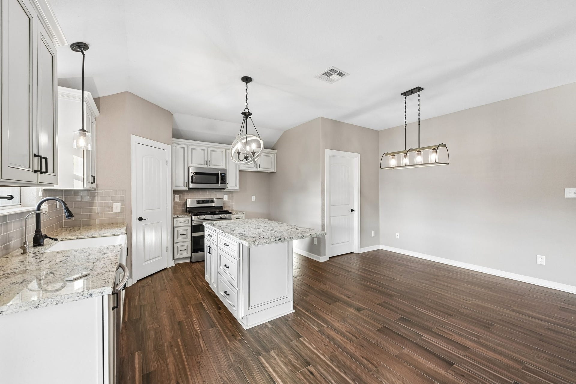 5012 Bayou Dr, Dickinson, TX 77539 Modern kitchen with elegant granite countertops, stainless steel appliances, and stylish pendant lighting, seamlessly flowing into a spacious living area with rich wood flooring.
