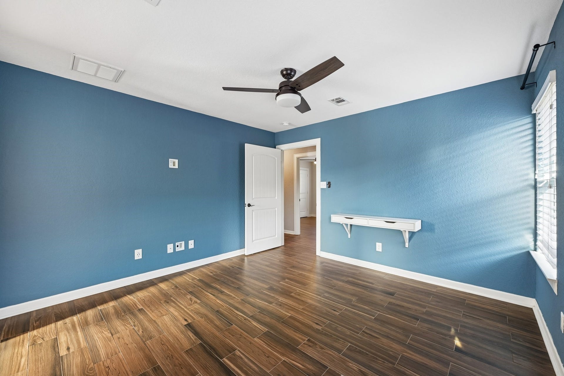 5012 Bayou Dr, Dickinson, TX 77539 Spacious room with rich wooden flooring and calming blue walls, featuring a modern ceiling fan and ample natural light from large windows.