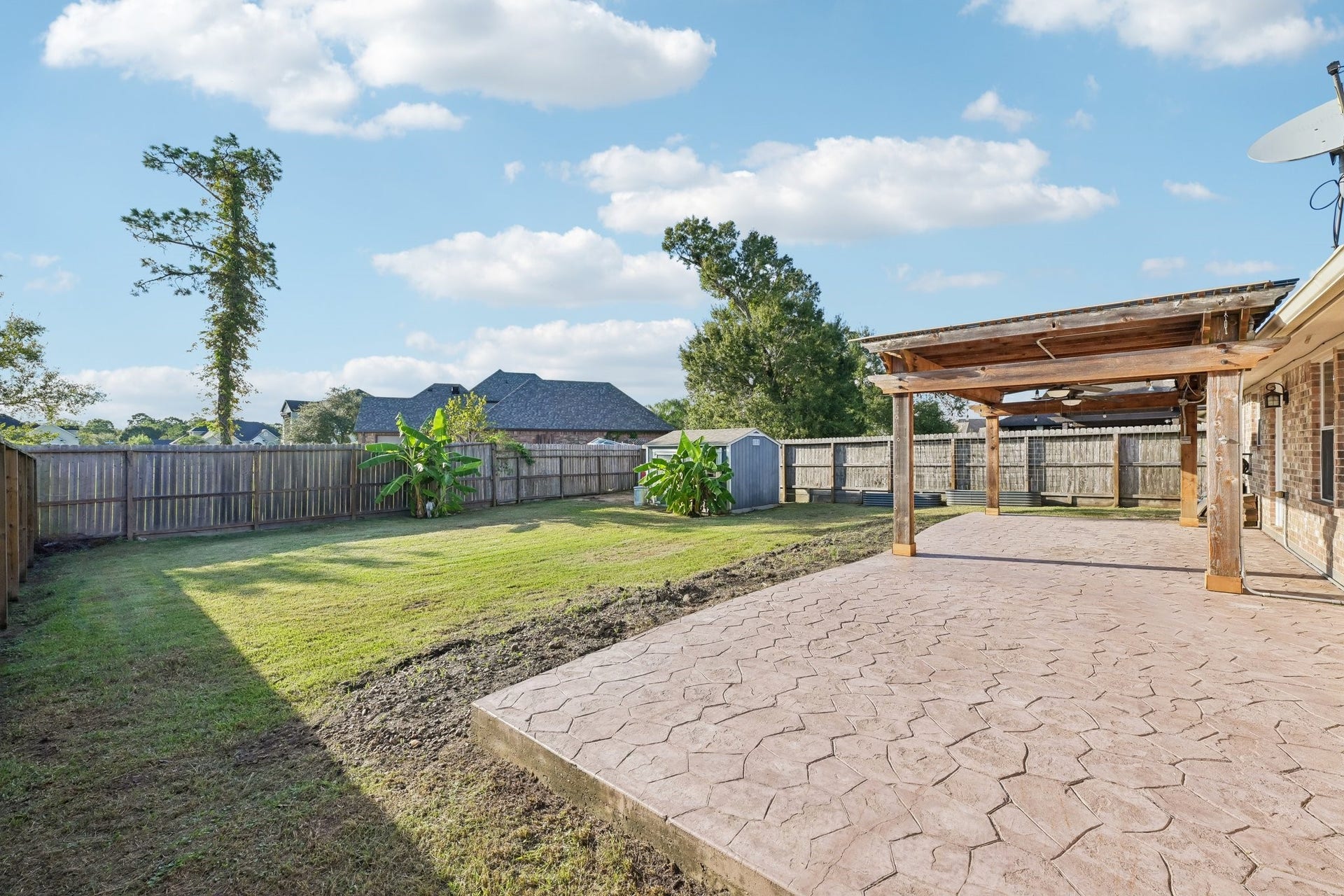 5012 Bayou Dr, Dickinson, TX 77539 Spacious backyard with a beautifully stamped concrete patio and a wooden pergola, perfect for outdoor gatherings.