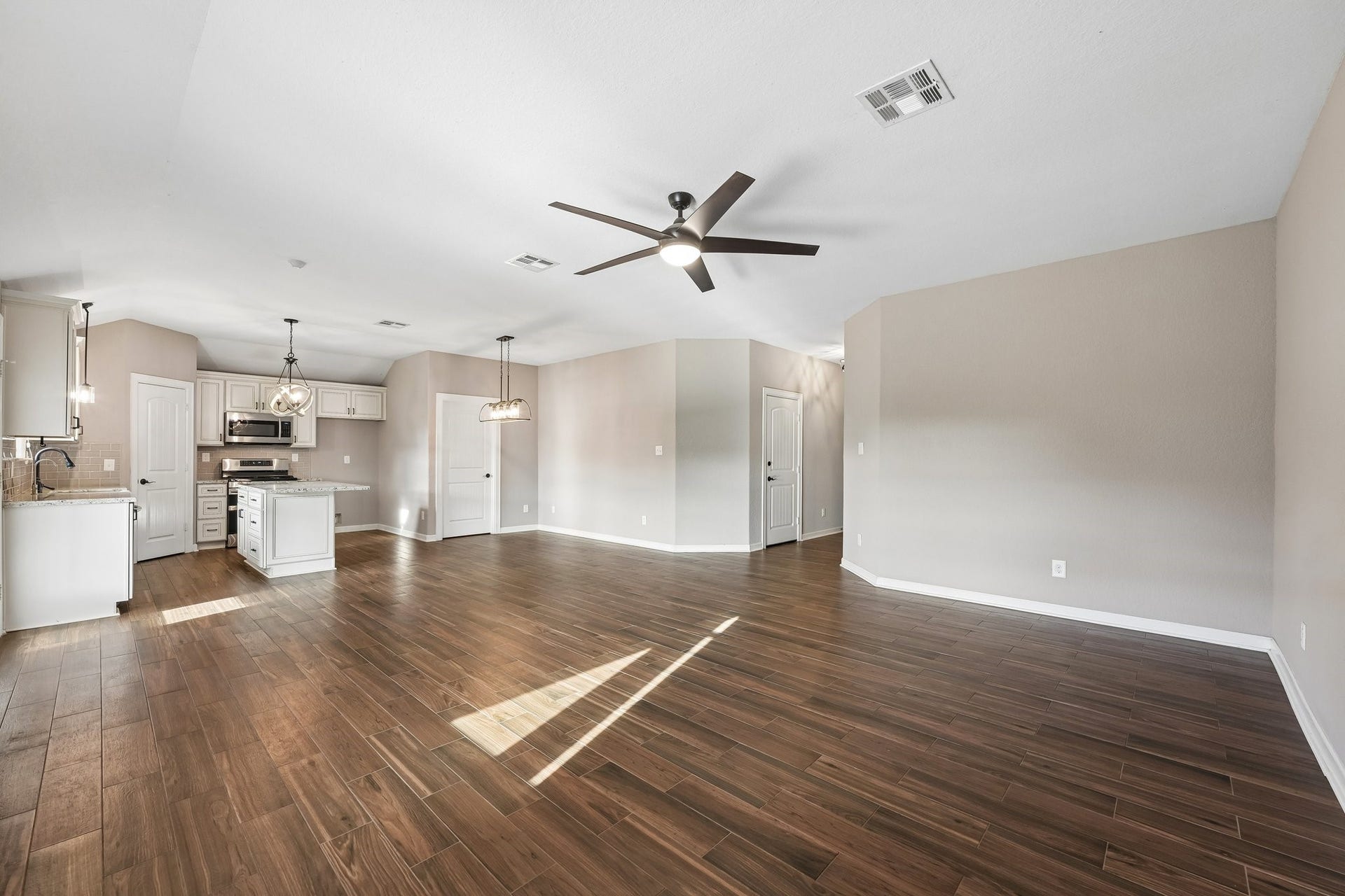 5012 Bayou Dr, Dickinson, TX 77539 Spacious open-concept living area with elegant wood flooring, modern ceiling fan, and a bright kitchen featuring stainless steel appliances and a central island.