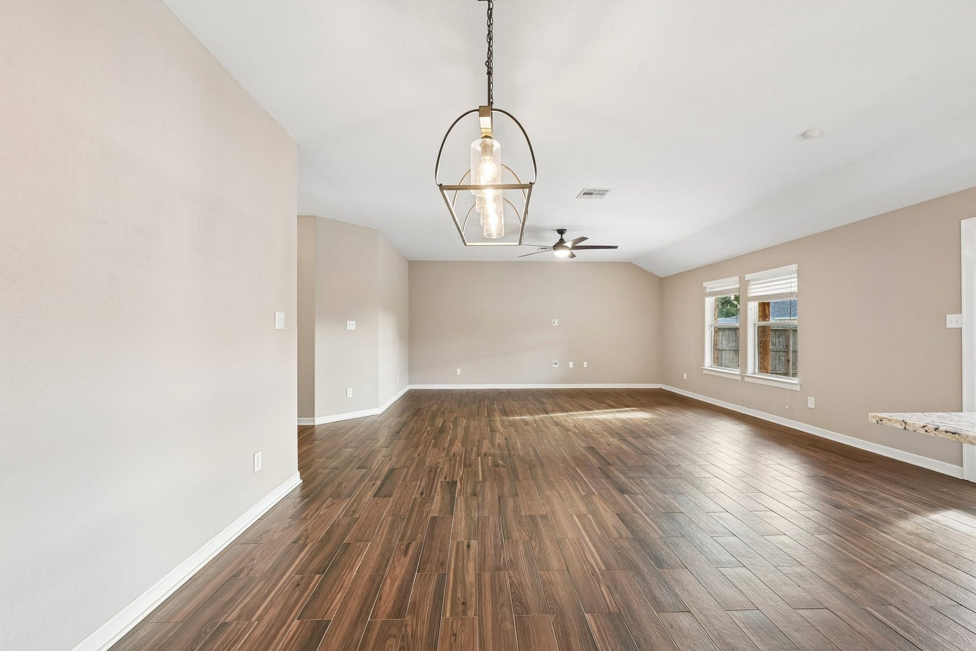 5012 Bayou Dr, Dickinson, TX 77539 Spacious living area with elegant wood flooring, modern light fixture, and abundant natural light from large windows.