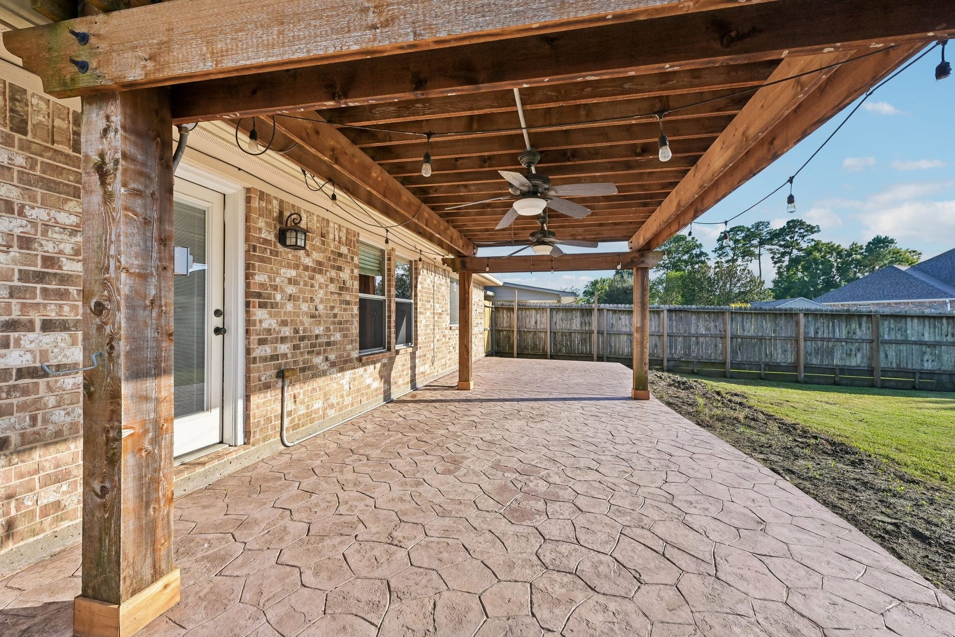 5012 Bayou Dr, Dickinson, TX 77539 Spacious covered patio with a stylish pergola, perfect for outdoor entertaining, featuring durable stamped concrete flooring and ceiling fans for added comfort.