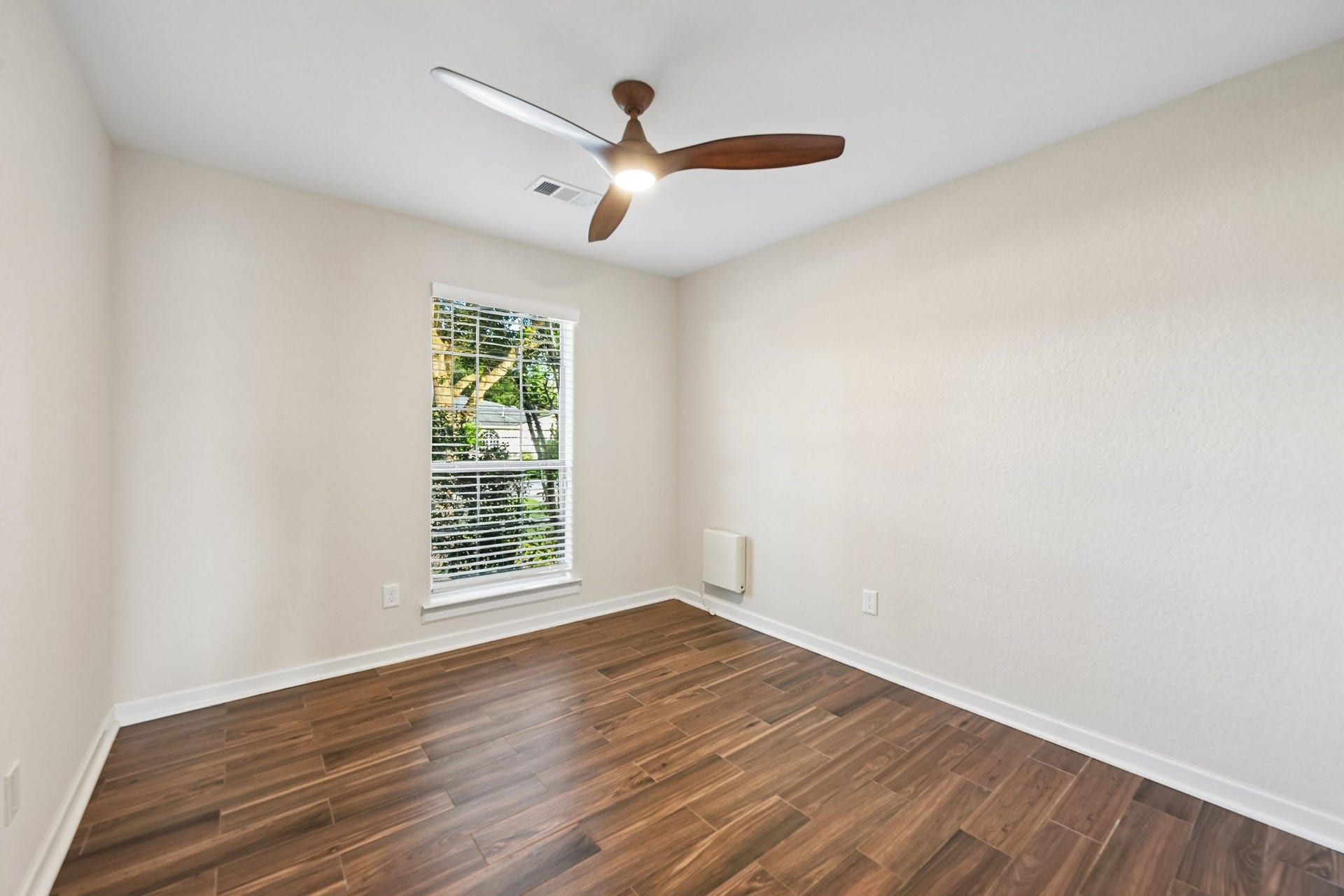 5012 Bayou Dr, Dickinson, TX 77539 Bright and inviting room with sleek wood flooring, a modern ceiling fan, and a large window providing ample natural light.
