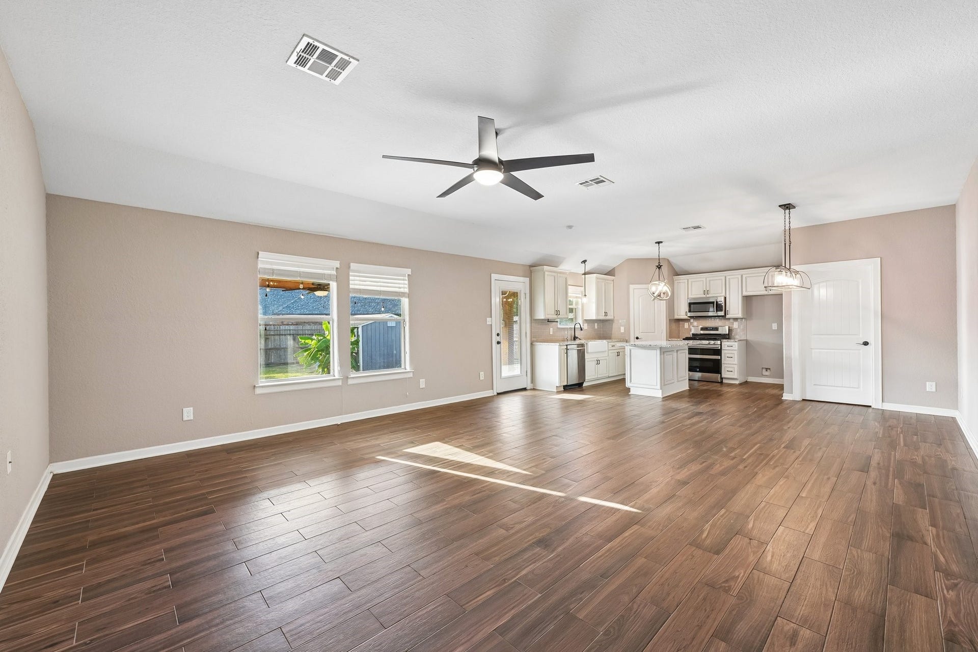 5012 Bayou Dr, Dickinson, TX 77539 Spacious open-concept living area with elegant wood-look flooring, modern ceiling fan, and a stylish kitchen featuring white cabinetry, stainless steel appliances, and pendant lighting.