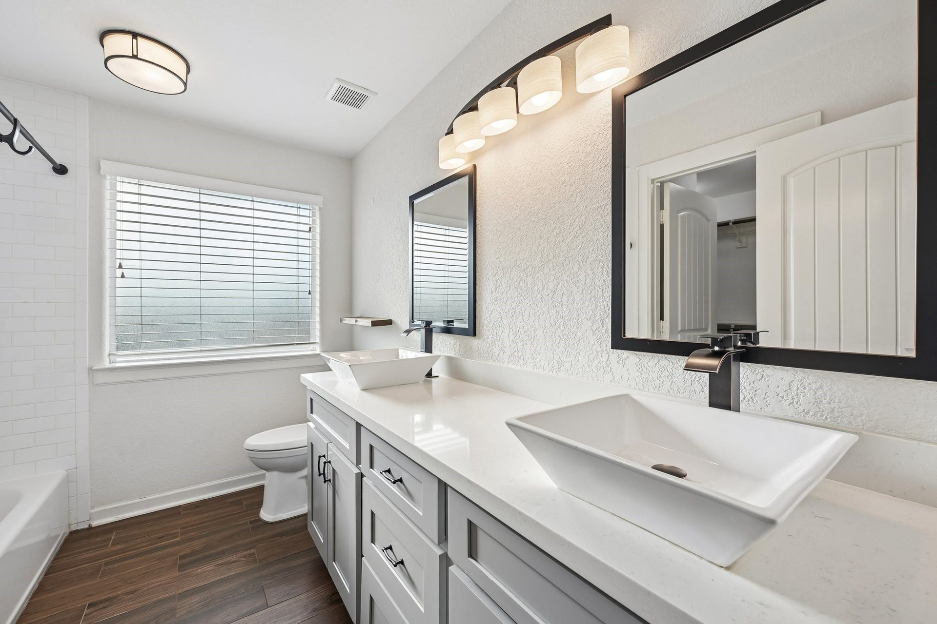 5012 Bayou Dr, Dickinson, TX 77539 Bright and modern bathroom featuring dual vessel sinks, sleek black fixtures, and elegant lighting, complemented by wood-look tile flooring and a spacious vanity.